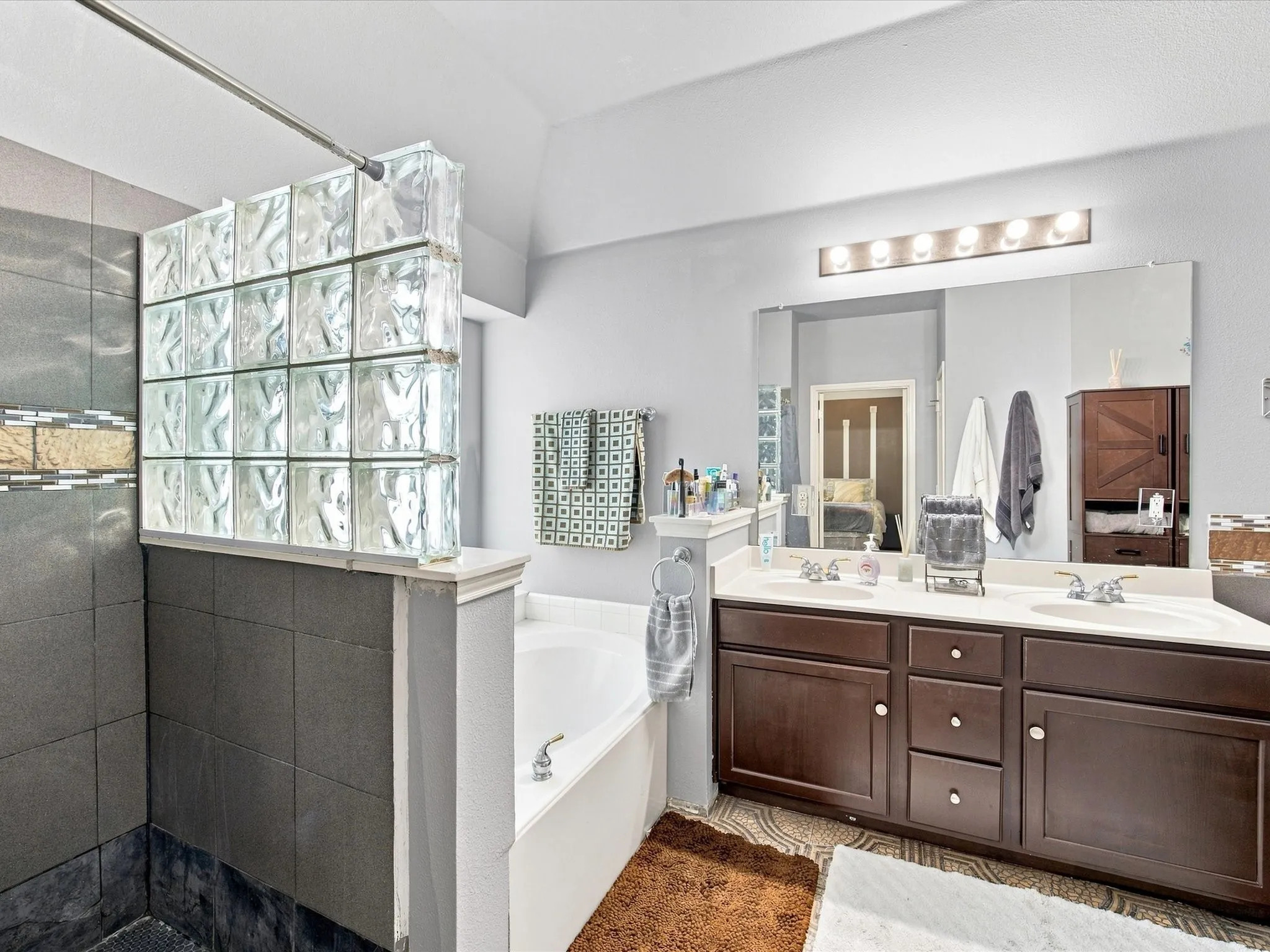 Dual sink vanity with dark wood-finish cabinetry, a large built-in mirror, and overhead strip lighting