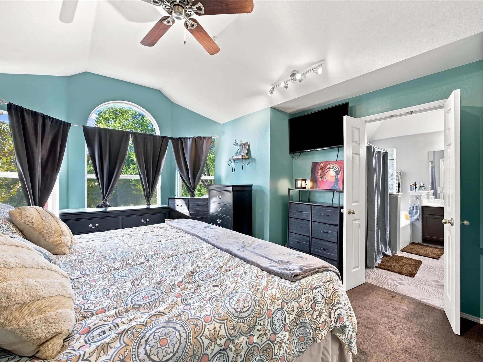 Vaulted ceiling with a ceiling fan, arched window, and track lighting