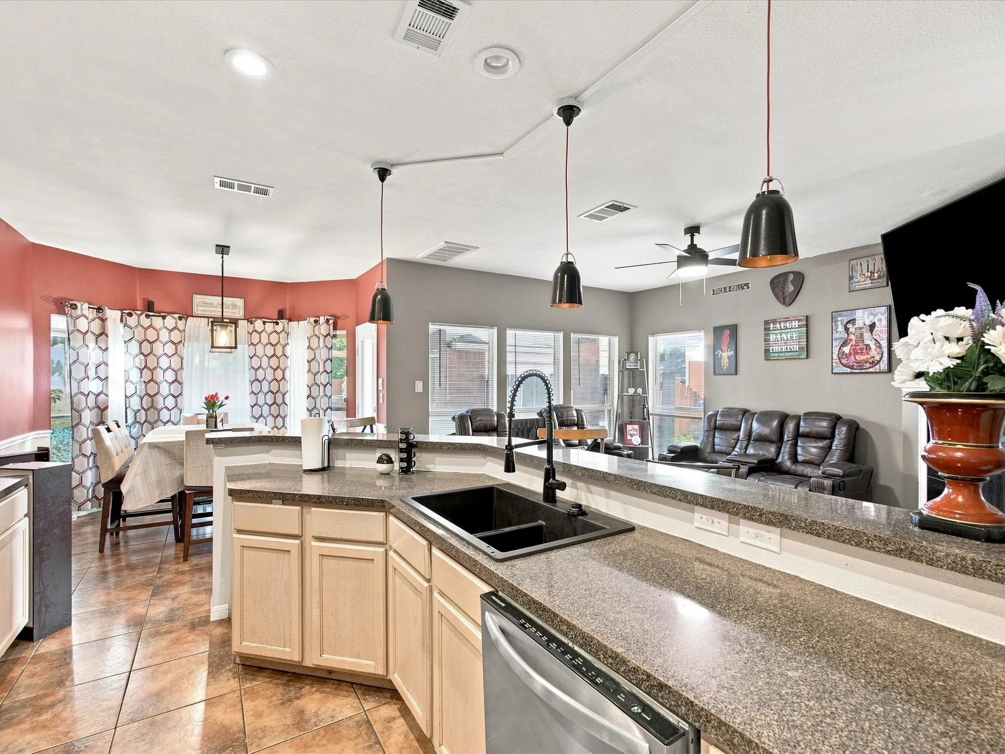 Kitchen with dark granite-style countertops, light wood-finish cabinetry, a black composite sink, and a stainless steel dishwasher
