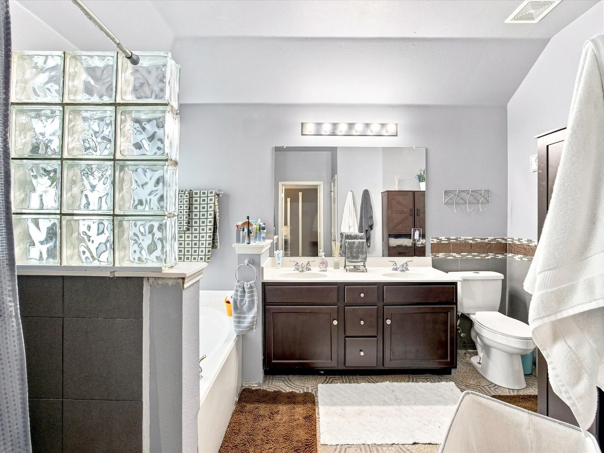 Dual sink vanity with dark wood-finish cabinetry, a large wall-mounted mirror, and overhead strip lighting
