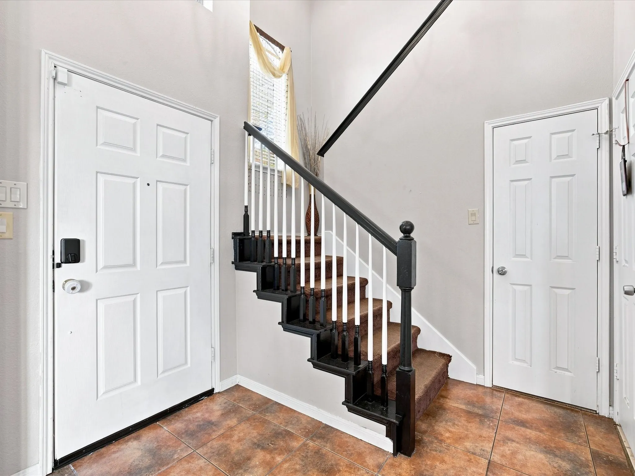 Elegant foyer showcasing a striking staircase with black-painted treads, white spindles, and brass handrail accents
