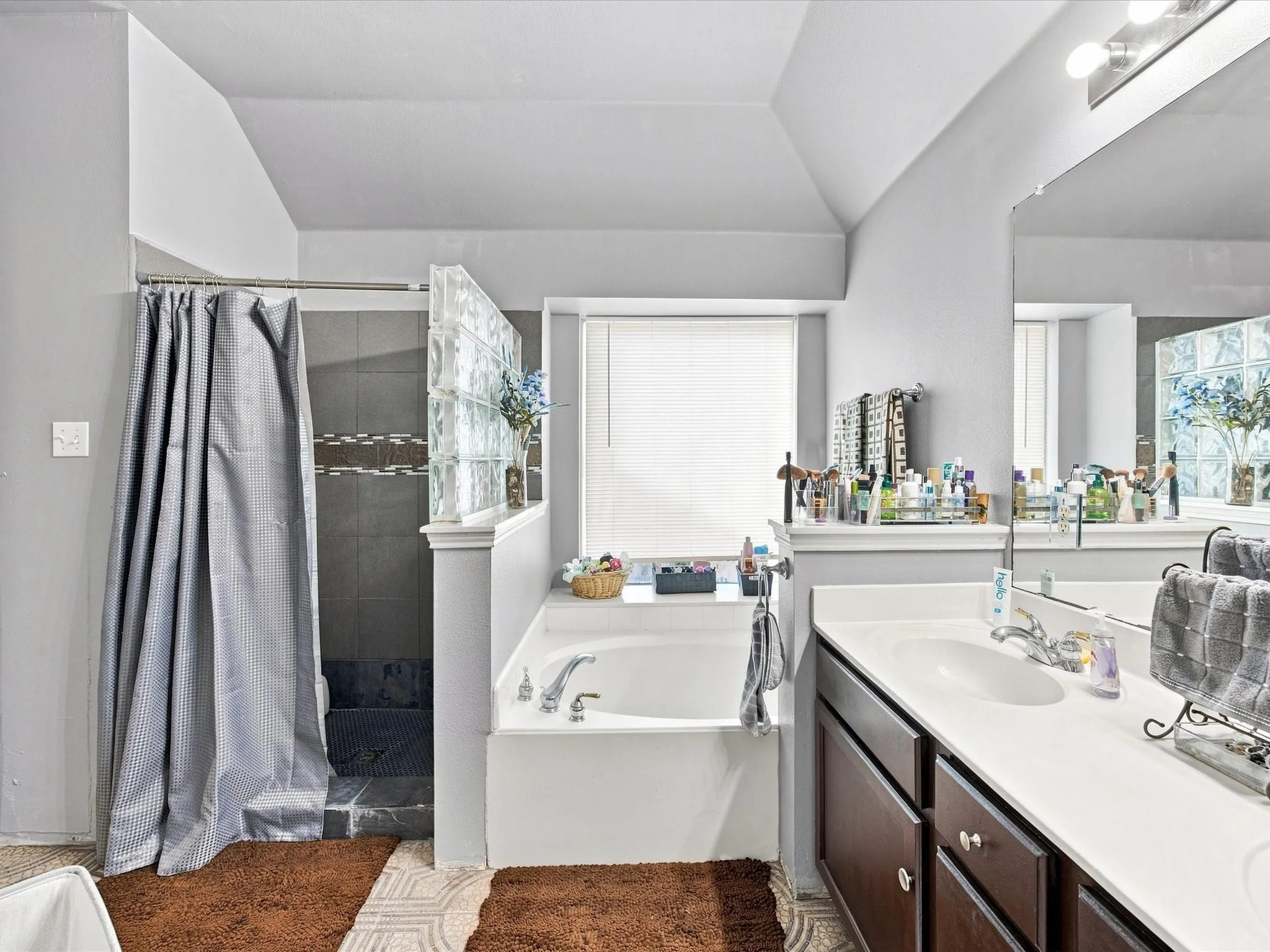Double vanity with white countertop, integrated bathtub, shower with glass block partition, and textured shower tile
