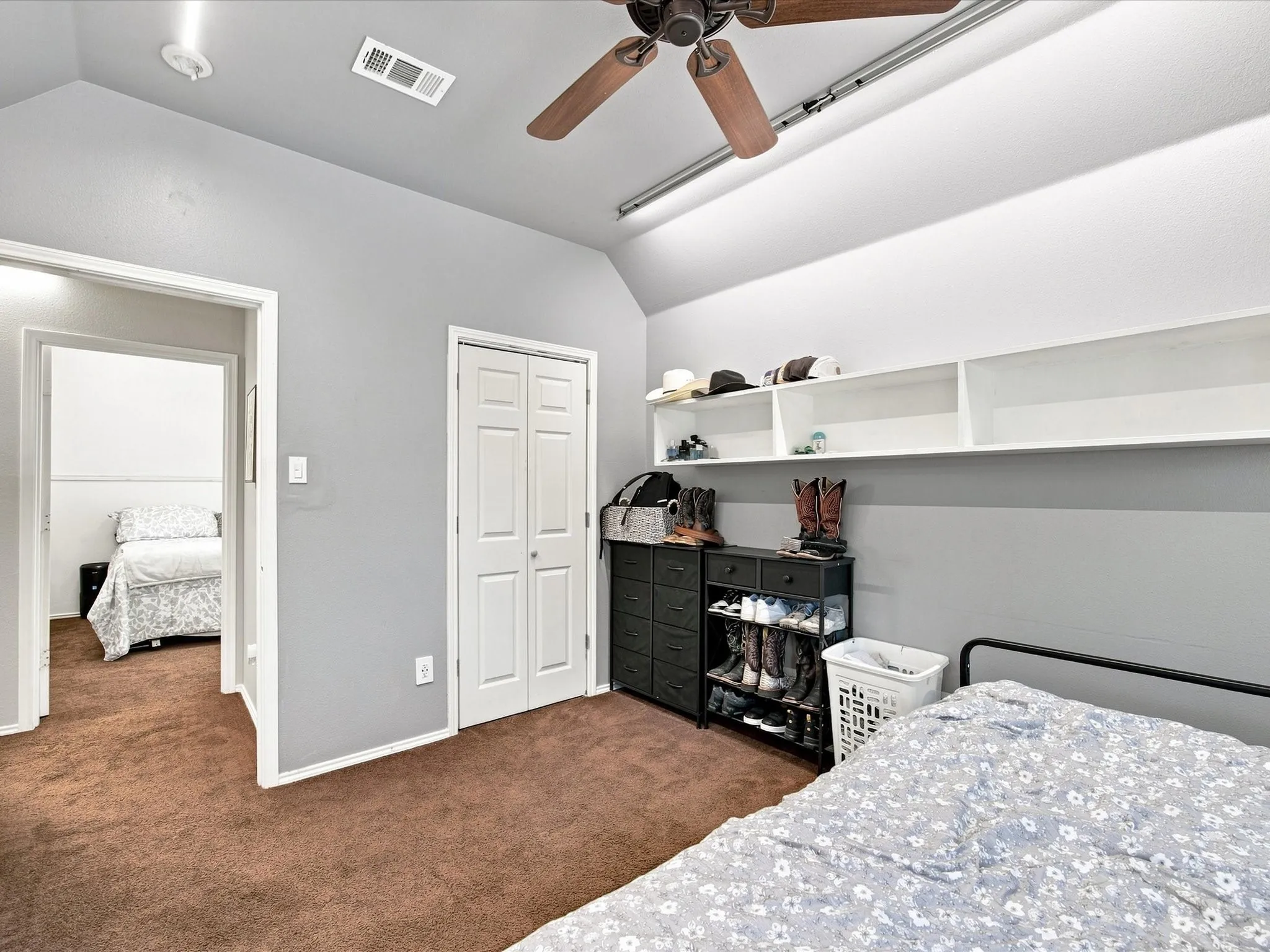 Sloped ceiling with a ceiling fan, light gray wall paint, brown carpet flooring, and white bifold closet doors