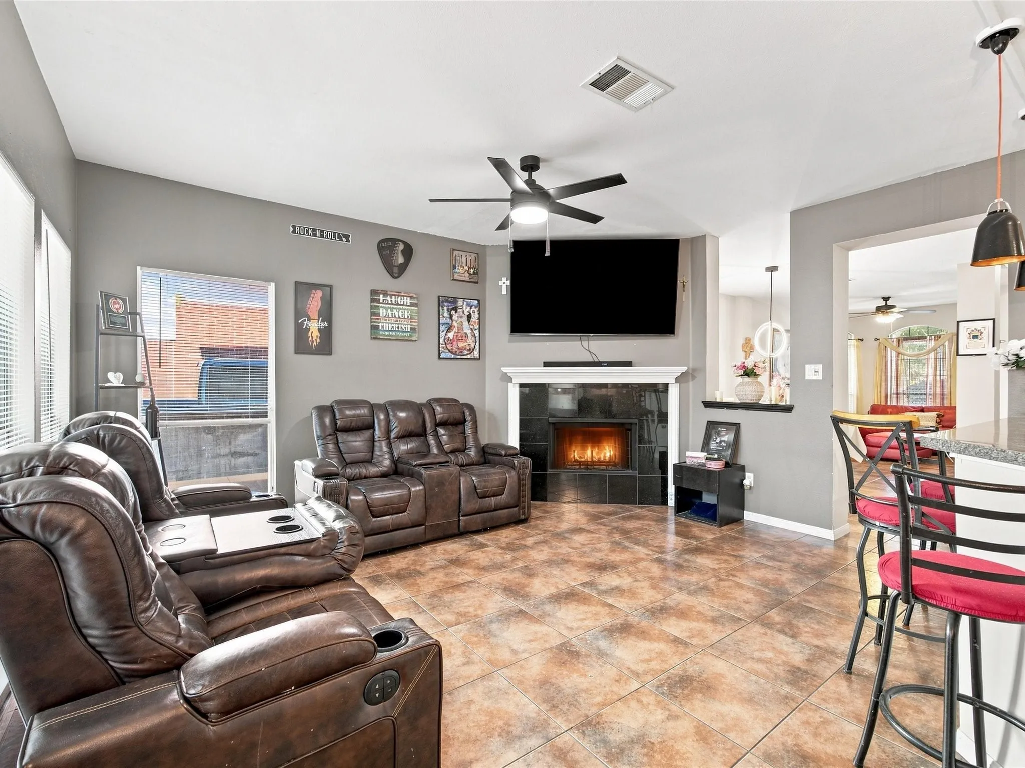 Spacious living area featuring a fireplace with a black tile surround, a ceiling fan, and large windows with blinds