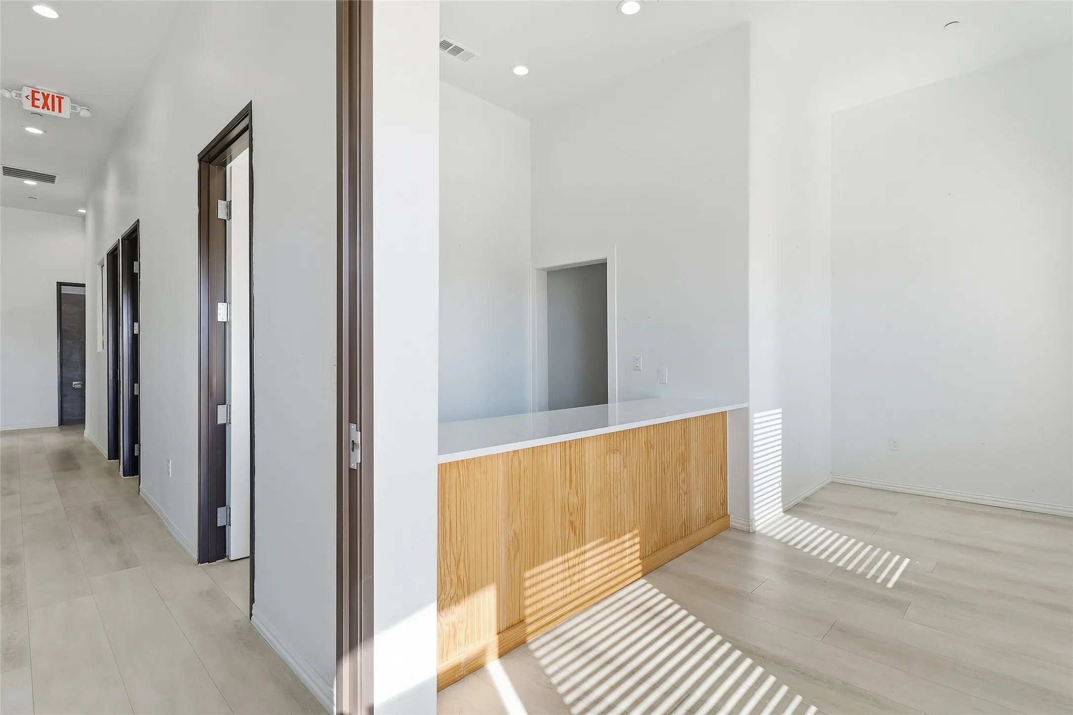 Recessed lighting, wood-finish flooring, white walls, wood-paneled counter with white surface, dark-framed doors