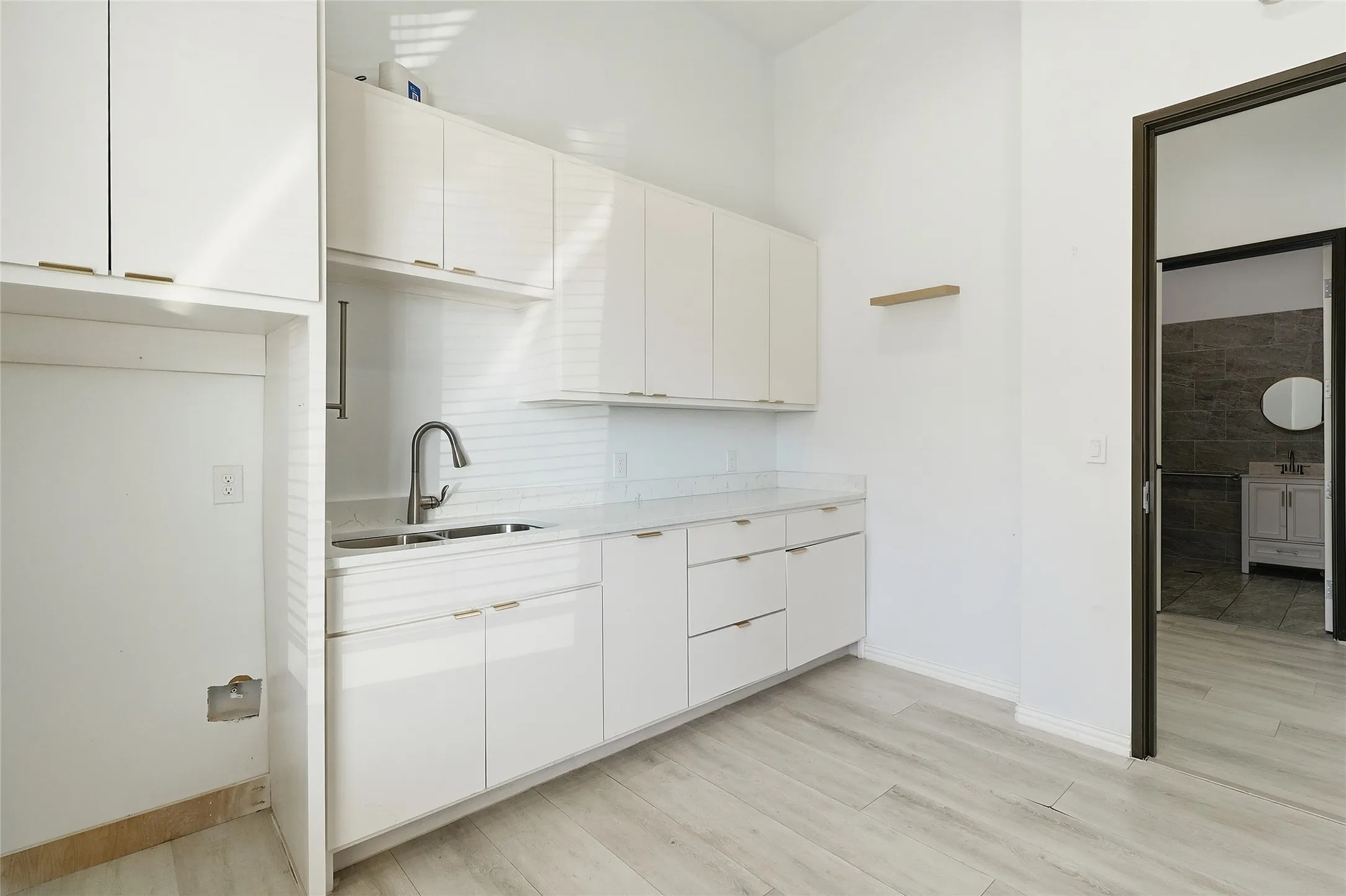 White cabinetry with gold-tone hardware, white countertop, stainless steel sink, and wood-finish flooring