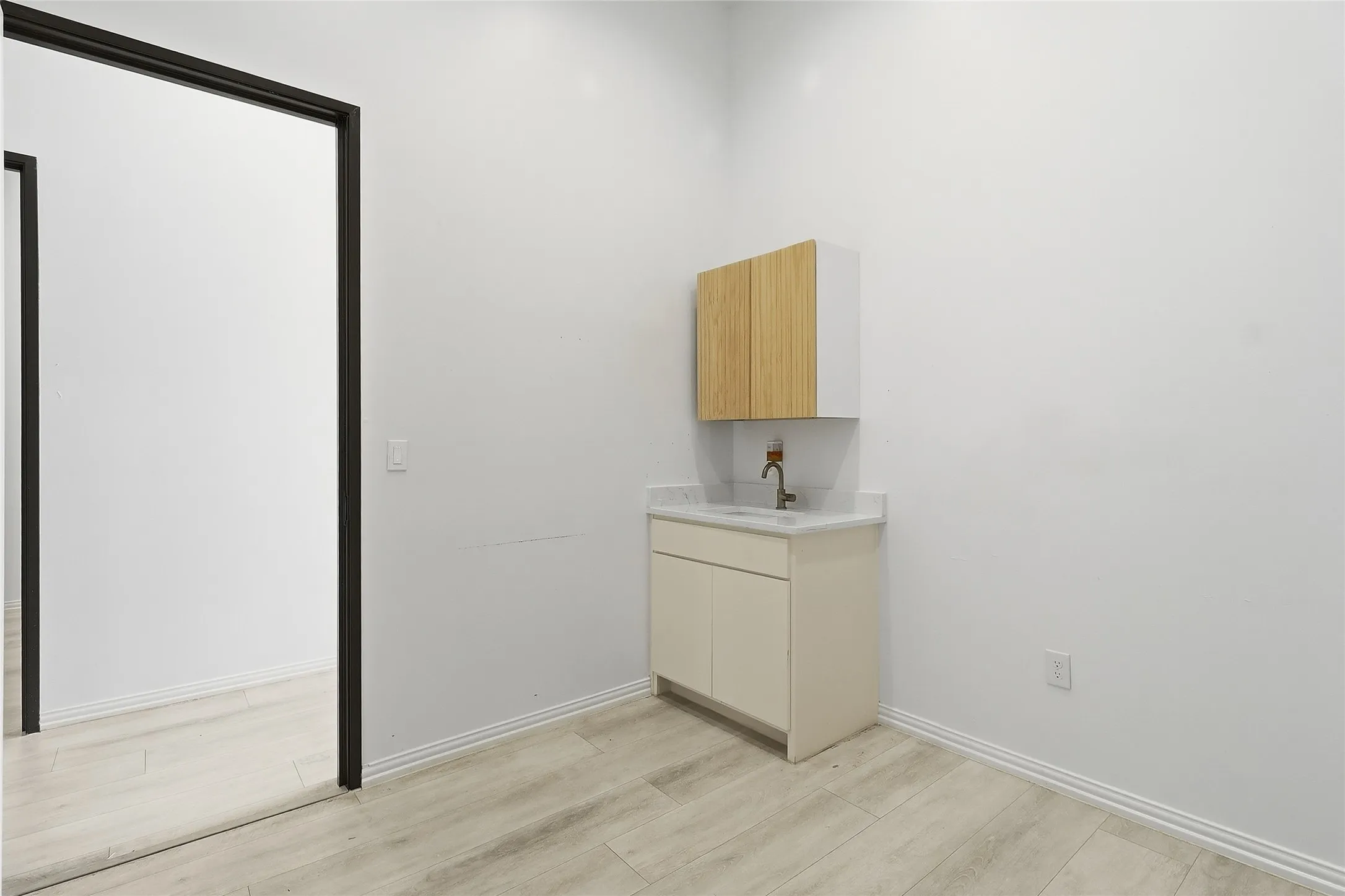 Light wood-finish flooring, built-in vanity with integrated sink, sleek countertop, and wall-mounted cabinetry with wood-panel doors