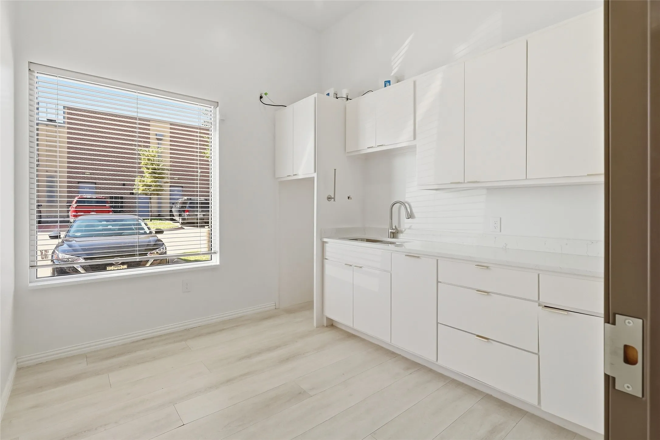 White cabinetry, stainless steel sink, white subway tile backsplash, light wood-finish flooring, and a large window with blinds