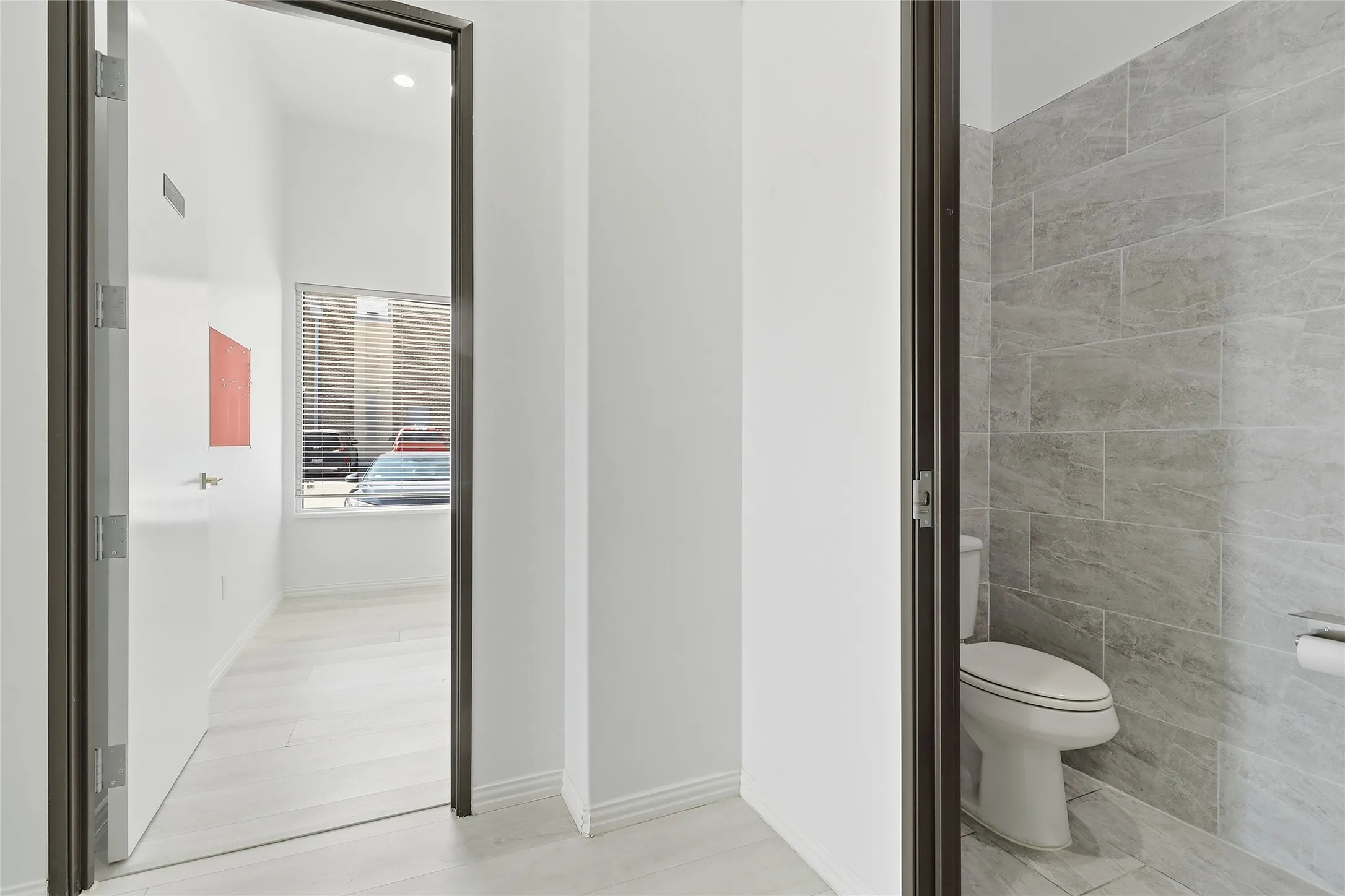 Recessed lighting, wood-finish flooring, white walls, window with horizontal blinds, and tiled bathroom walls