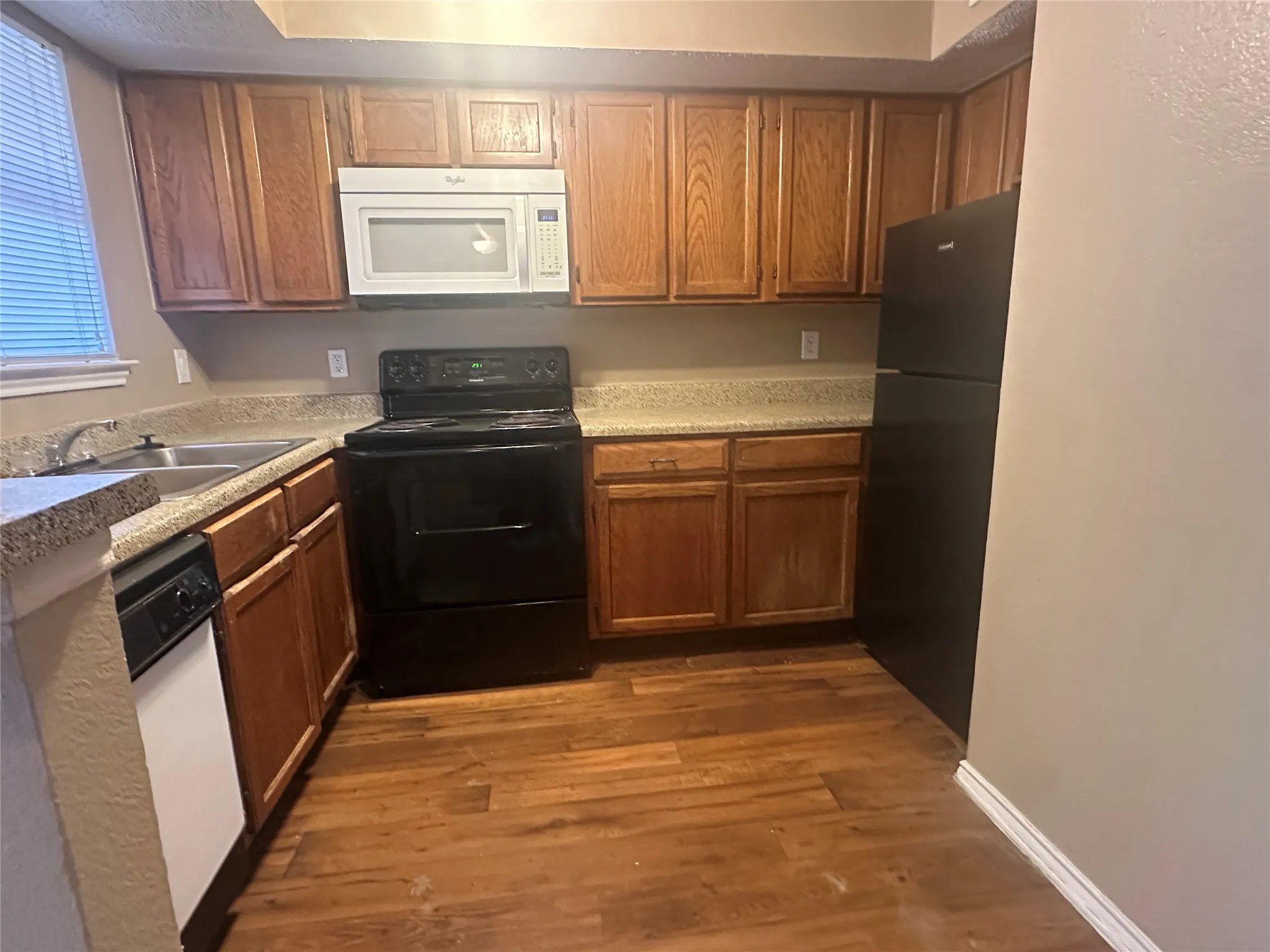 Kitchen featuring wood-finish flooring, wood cabinetry, a built-in microwave, and a stainless steel sink