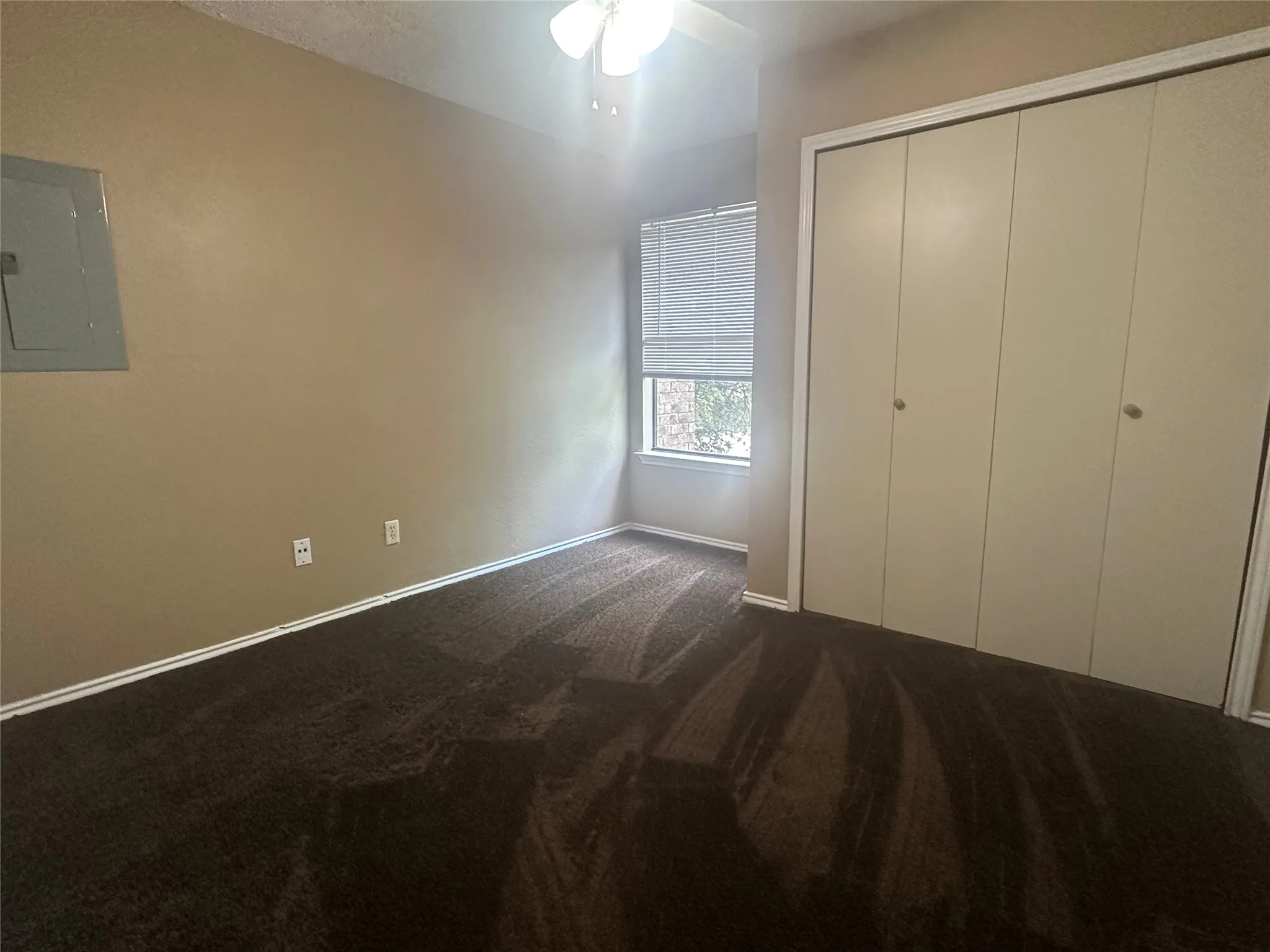Brown carpet flooring, neutral-toned walls, a ceiling fan with integrated lighting, a window with blinds, and bi-fold closet doors