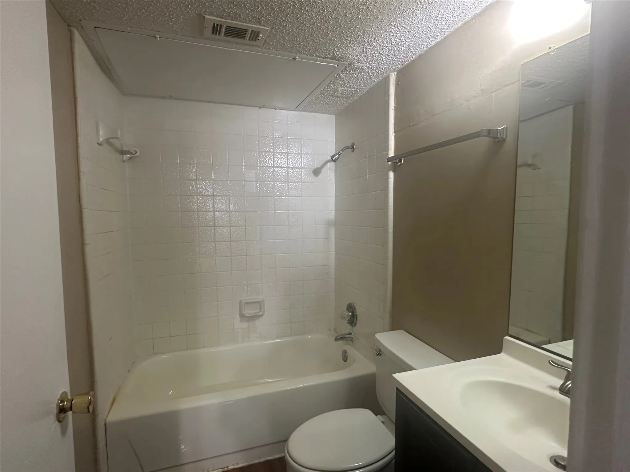 White tiled tub surround, white bathtub, wall-mounted mirror, vanity with an integrated sink, and a toilet
