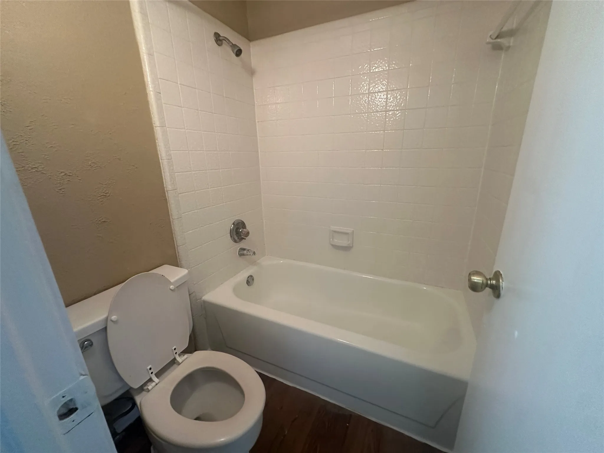 White tile shower surround, chrome shower fixtures, and wood-finish flooring