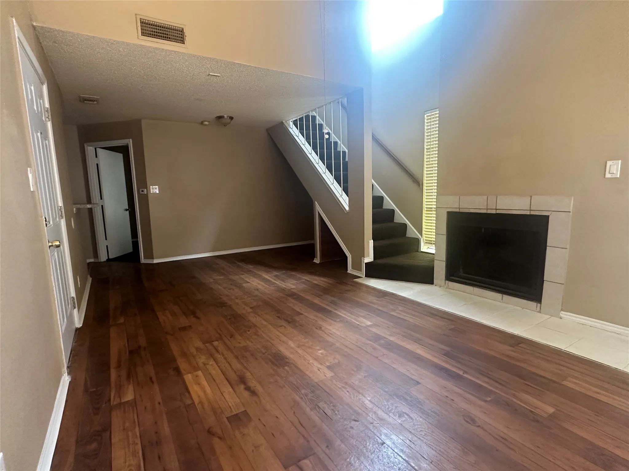 Hardwood-finish flooring, staircase with white railing, tiled fireplace, and neutral wall tones
