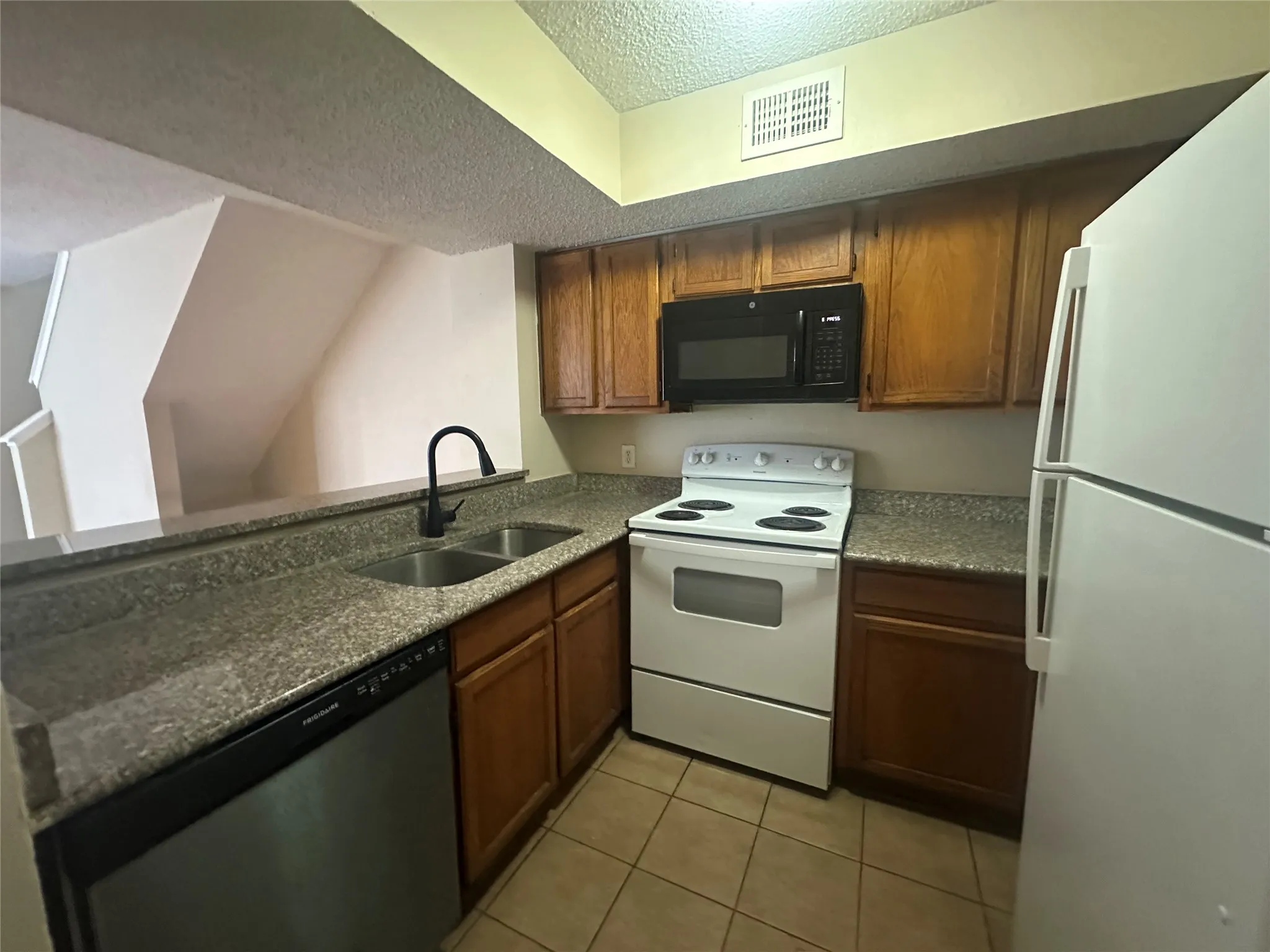 Kitchen featuring wood-finish cabinetry, granite-style countertops, stainless steel dual basin sink, and tile flooring