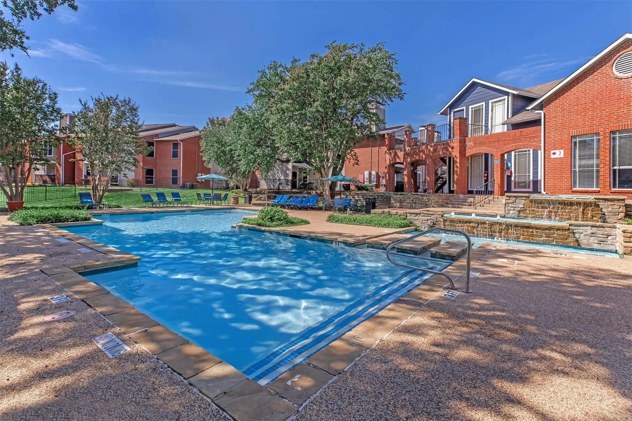 Outdoor swimming pool featuring a waterfall, integrated steps, and surrounding paved decking