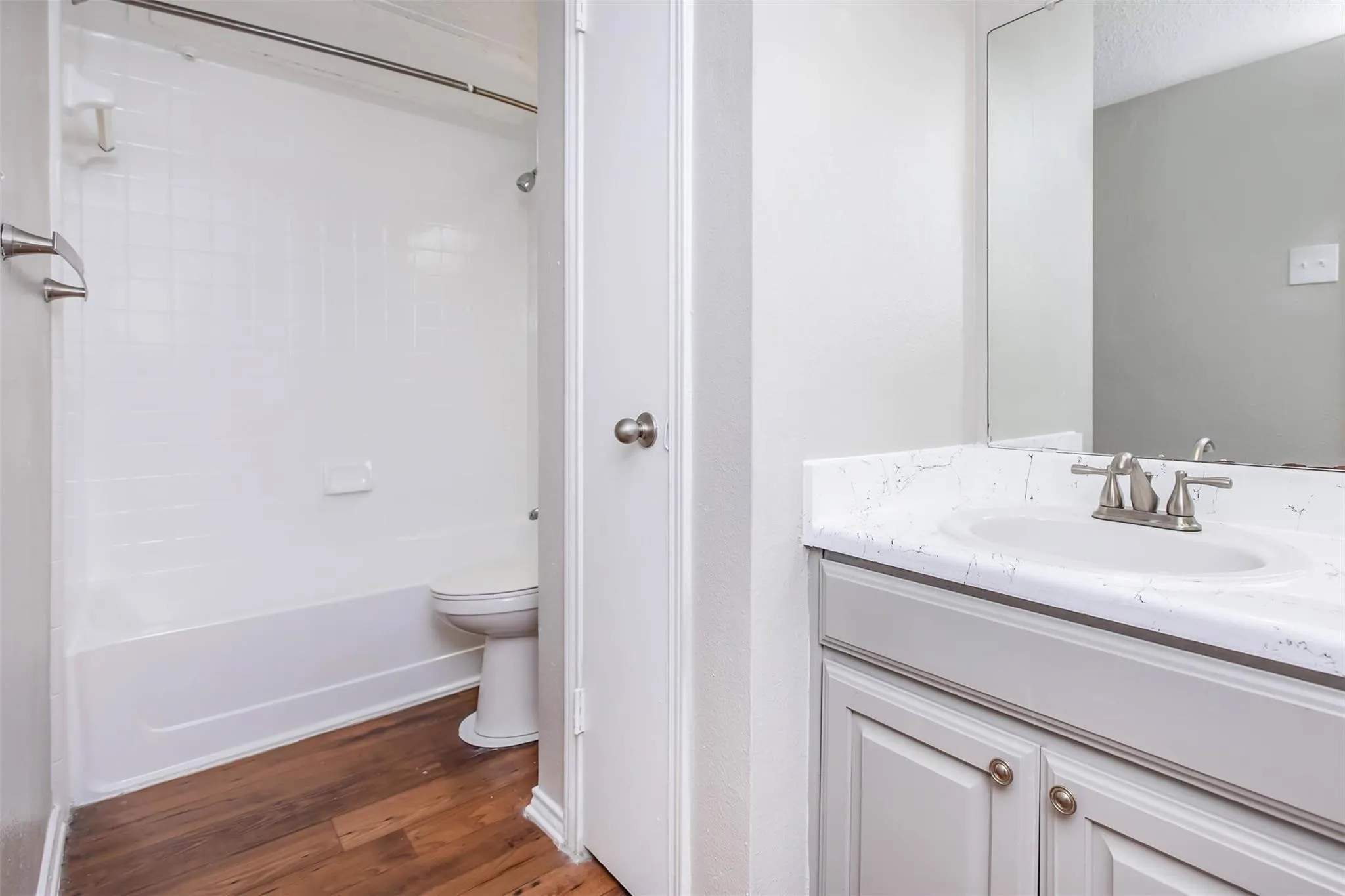 Bathroom featuring a tub/shower combination with white subway tile, wood-finish flooring, a vanity with a drop-in sink, and brushed nickel fixtures
