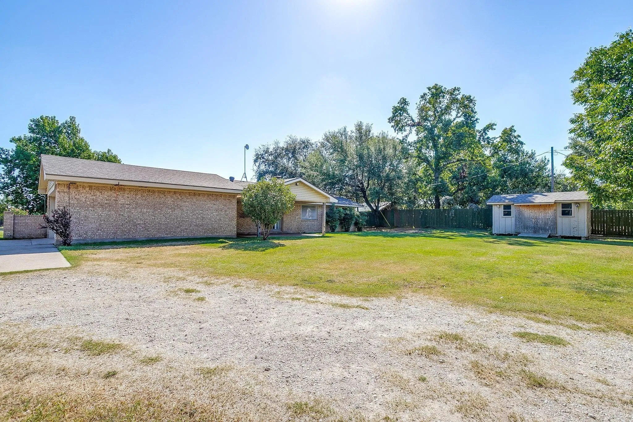 Expansive rear yard featuring green lawn, a detached storage shed, privacy fencing, and mature trees