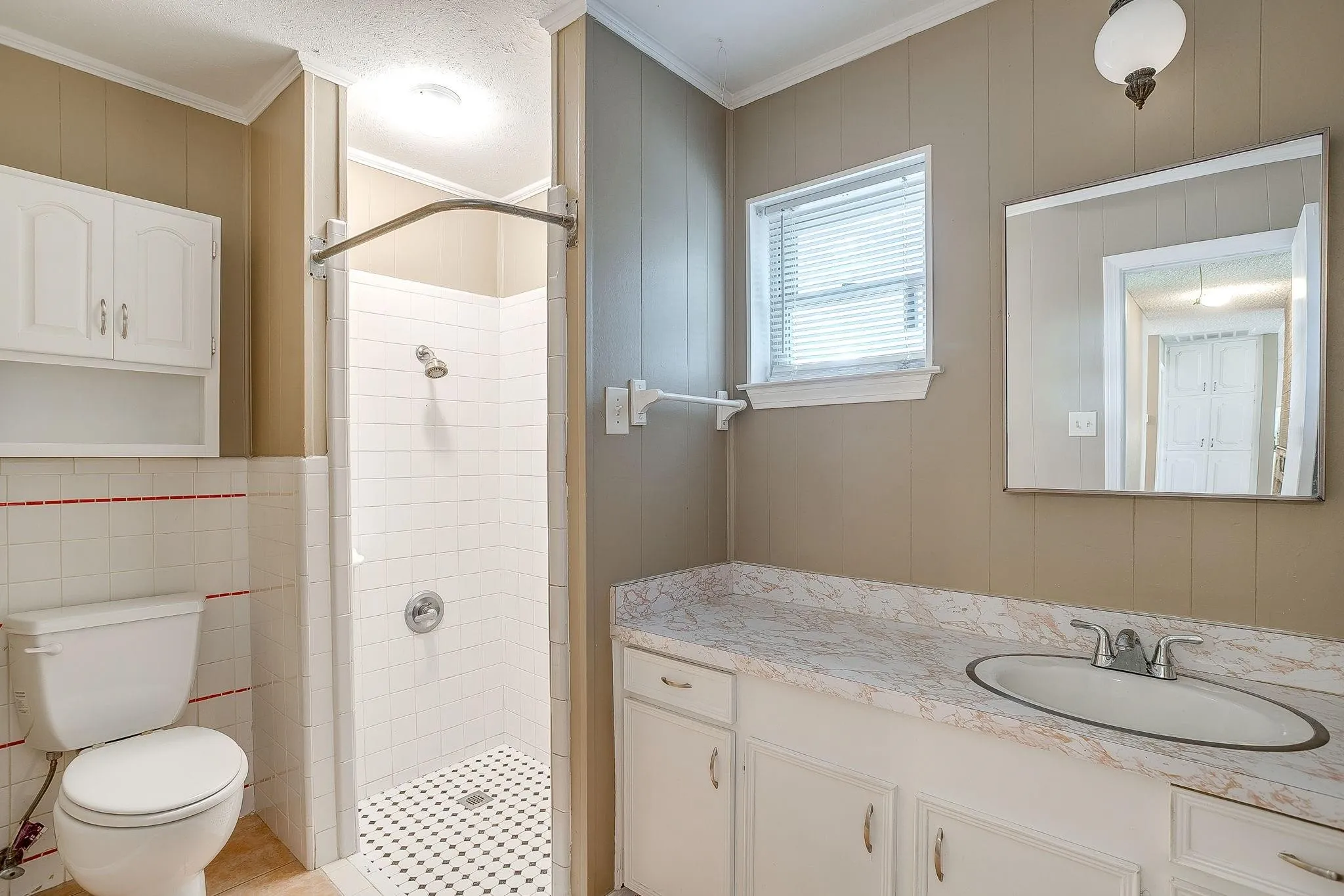 Walk-in shower with tile surround, vanity with an integrated sink, and wall-mounted storage cabinetry