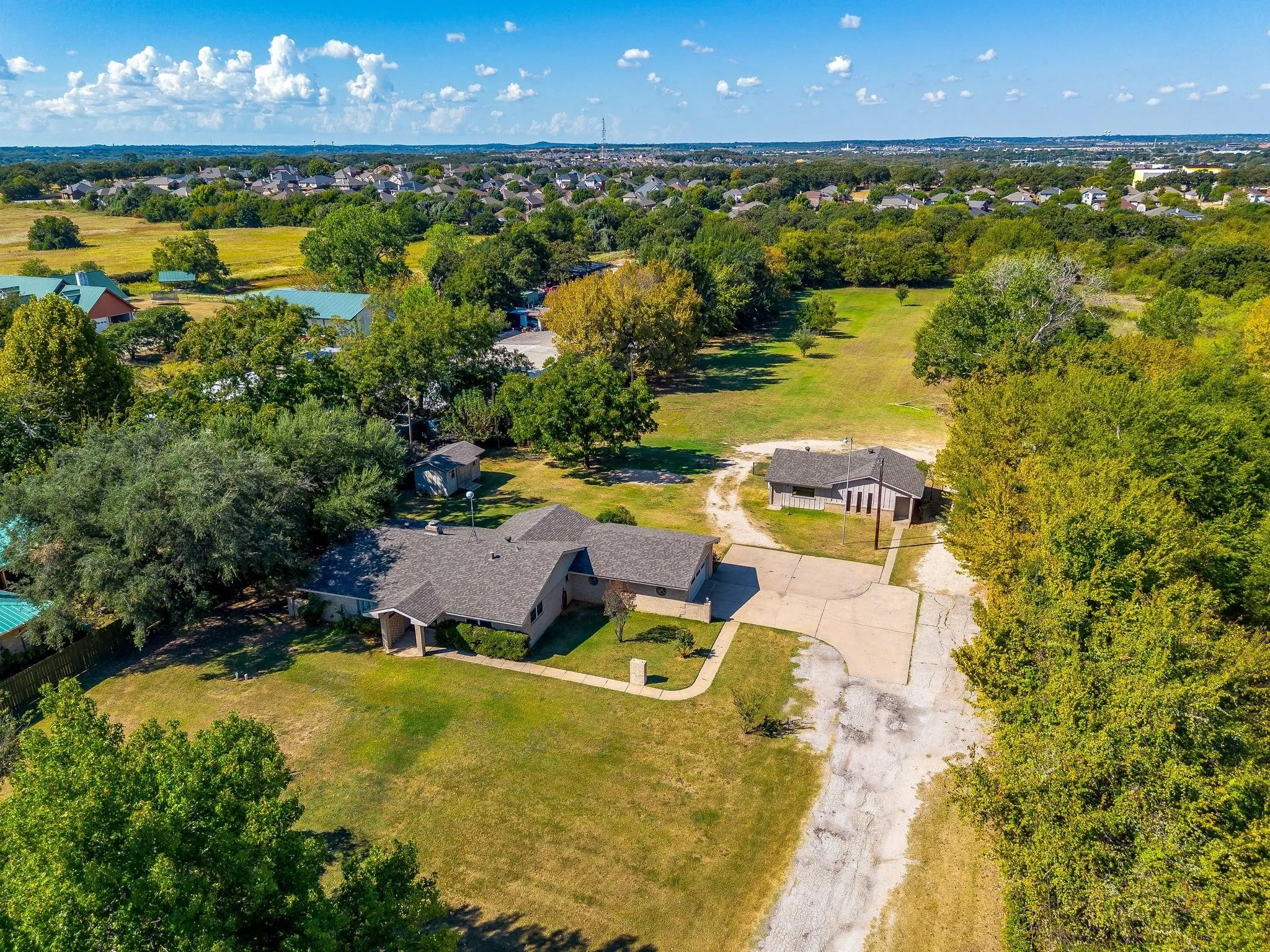 Spacious property featuring a main residence, an additional auxiliary structure, extensive paved driveway, and established trees across a large lot