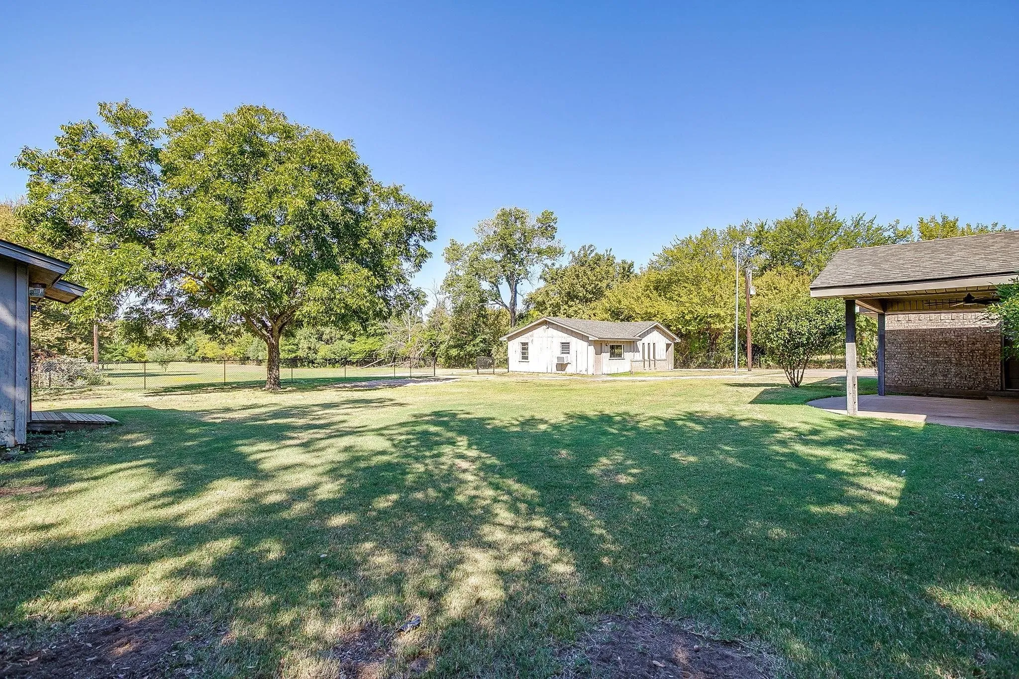 Expansive grassy yard with mature trees, fenced perimeter, and a detached outbuilding