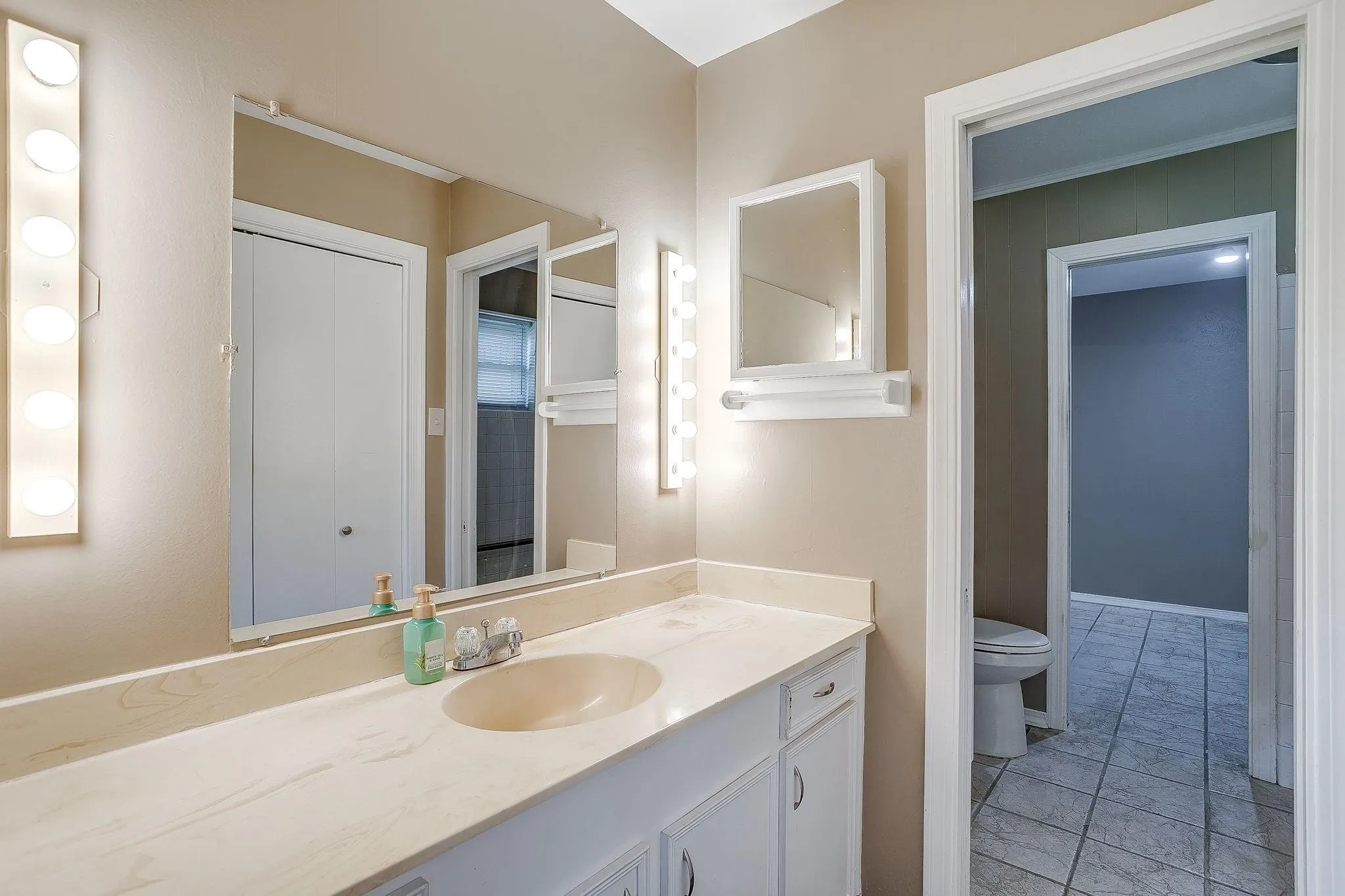 Vanity with an integrated sink, white cabinetry, wall-mounted light fixtures, and a mirrored medicine cabinet