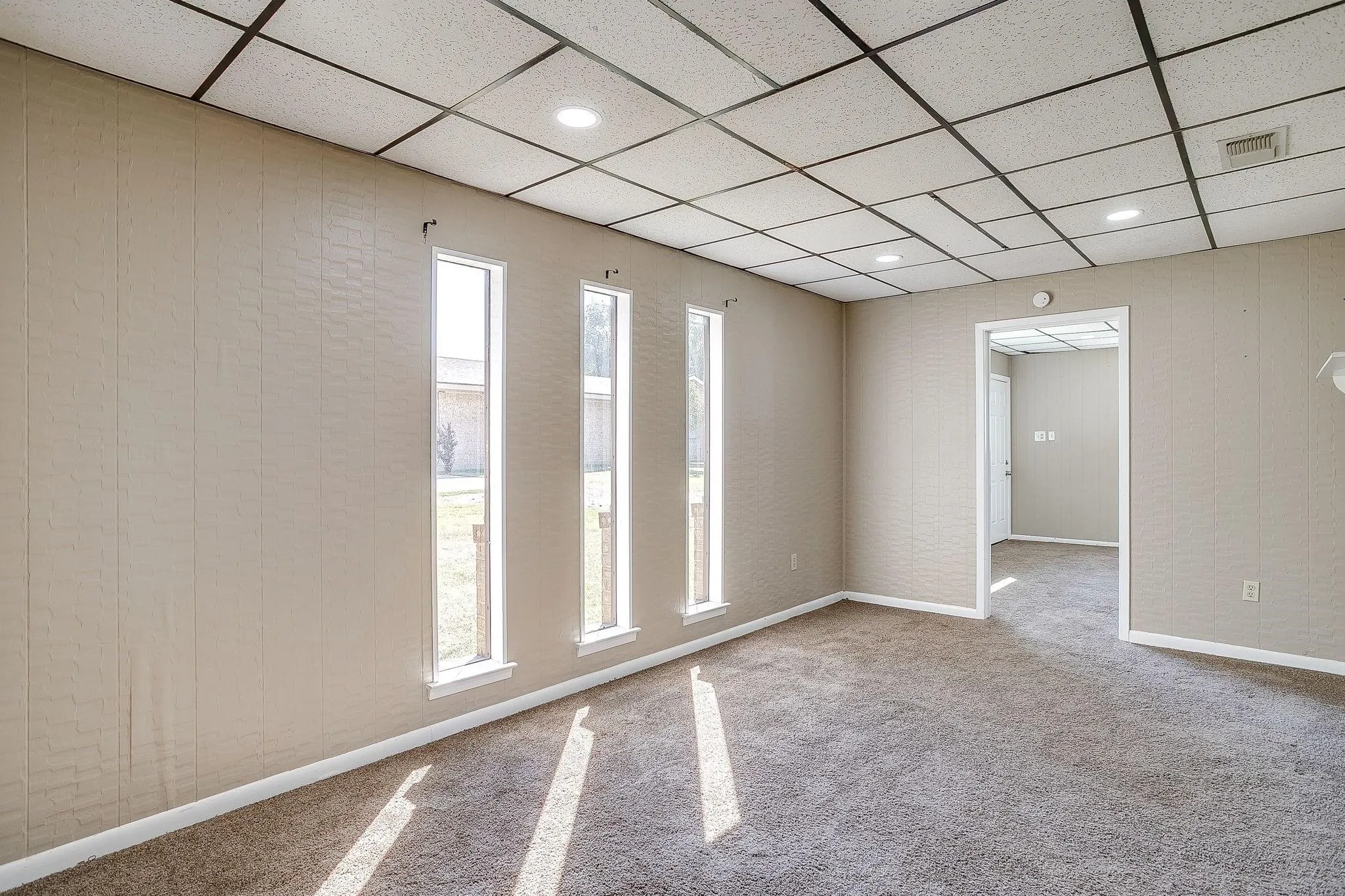 Recessed lighting, textured panel walls, three vertical windows, and wall-to-wall carpeting