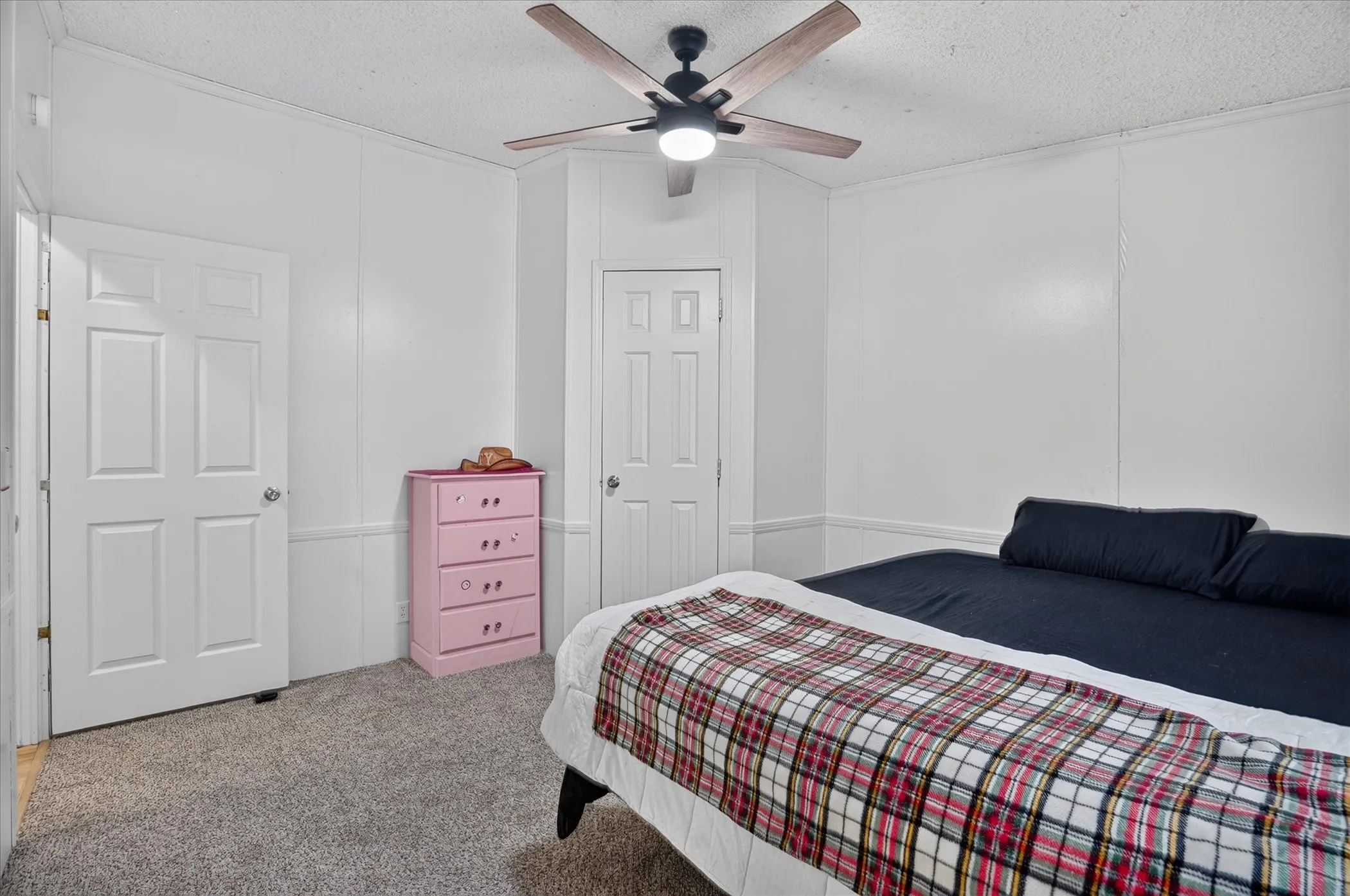 Textured ceiling, ceiling fan with light fixture, paneled walls, white interior doors, and gray carpeting