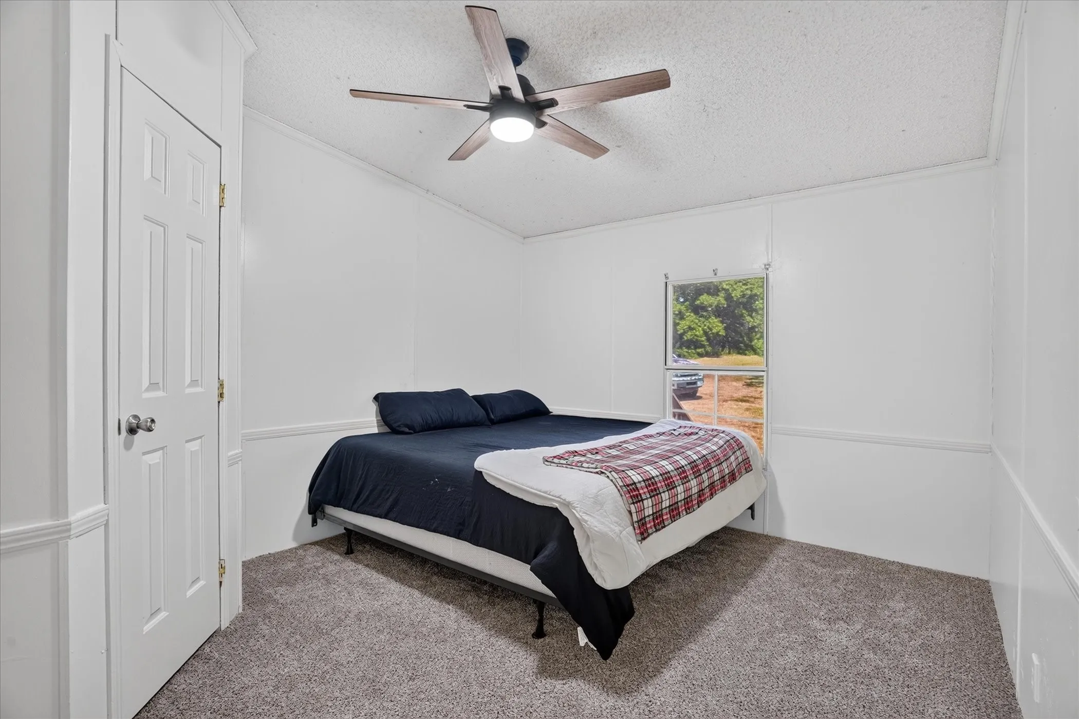 Carpeted flooring, white paneled walls, ceiling fan with integrated lighting, and a single window
