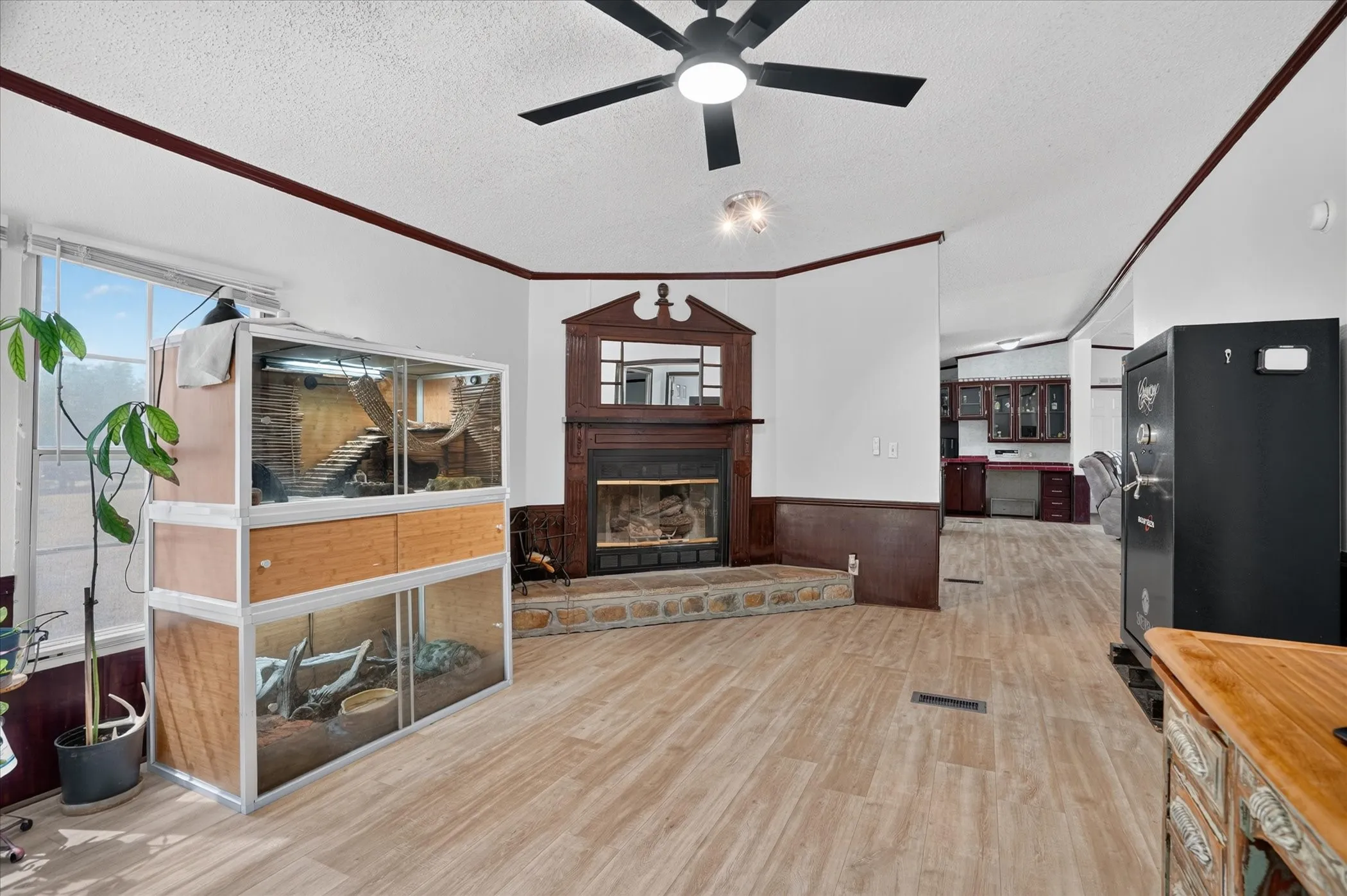 Living area featuring wood-finish flooring, a ceiling fan, and a fireplace with a stone hearth and wood surround