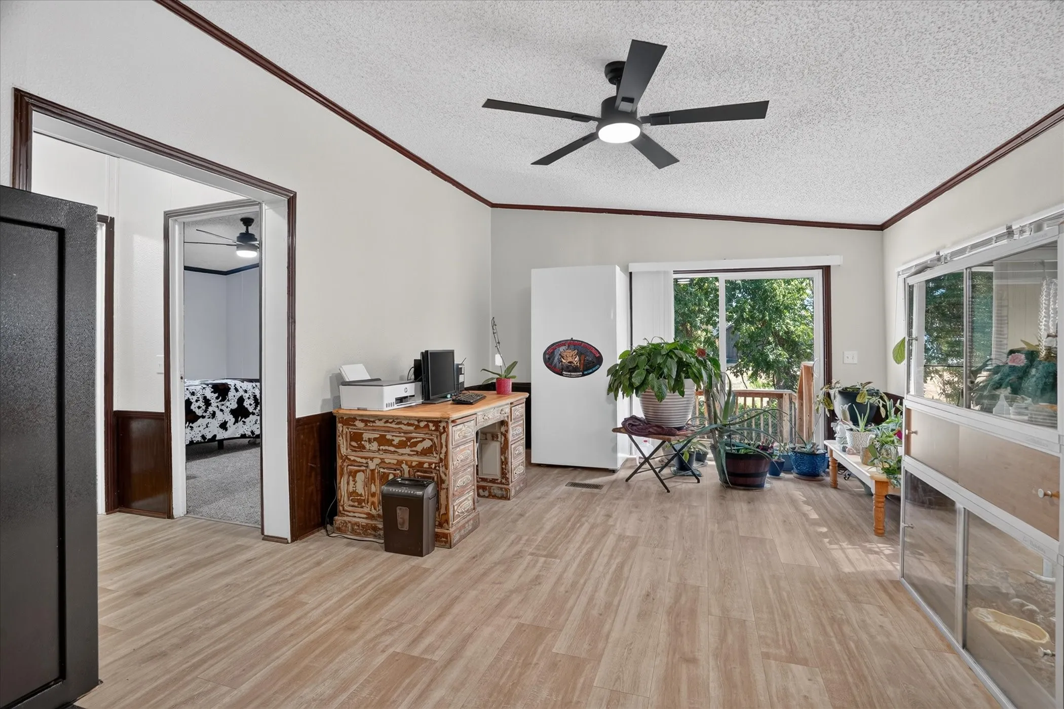Wood-finish flooring, ceiling fan with integrated lighting, sliding glass door, and white walls with wood trim