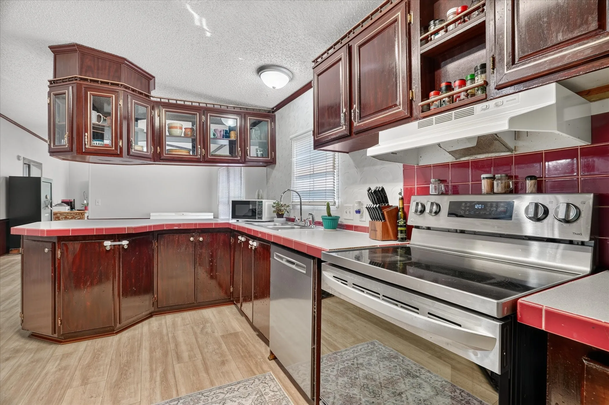Kitchen with wood-finish flooring, dark wood cabinetry, white countertops, and a red tile backsplash
