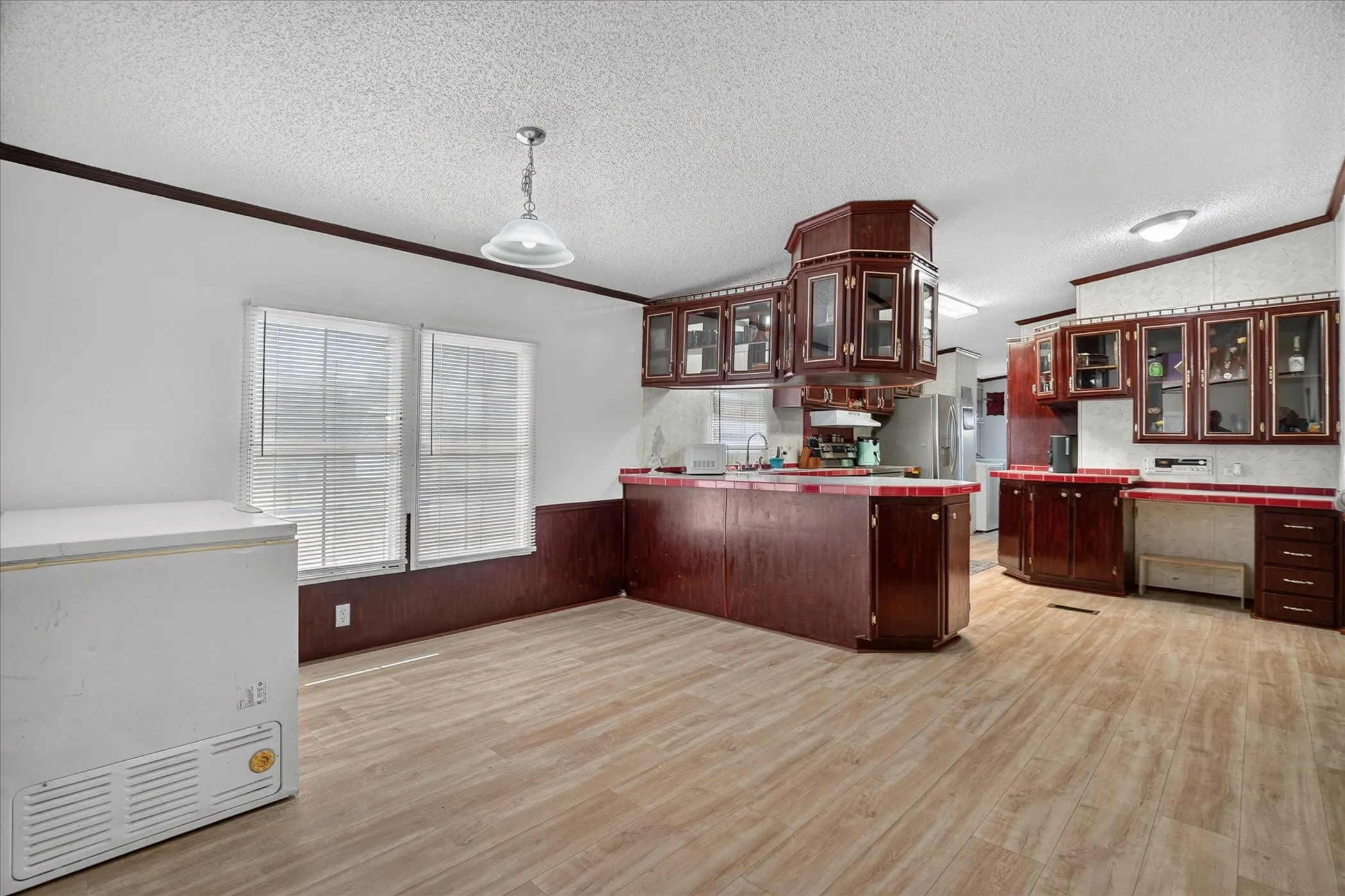 Kitchen featuring wood-finish flooring, dark wood cabinetry with glass-front uppers, and red tile​​‌​​​​‌​​‌‌​‌‌​​​‌‌​‌​‌​‌​​​‌​​ countertops