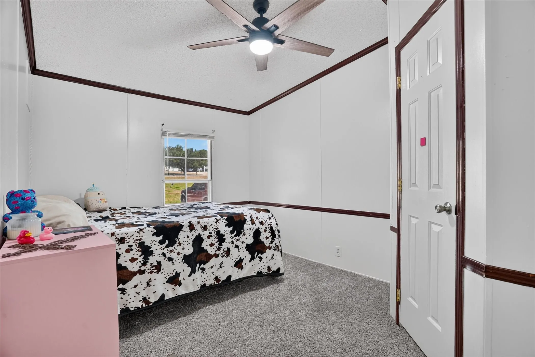 Recessed window, paneled interior walls, ceiling fan with integrated lighting, door with knob hardware, and gray carpeting