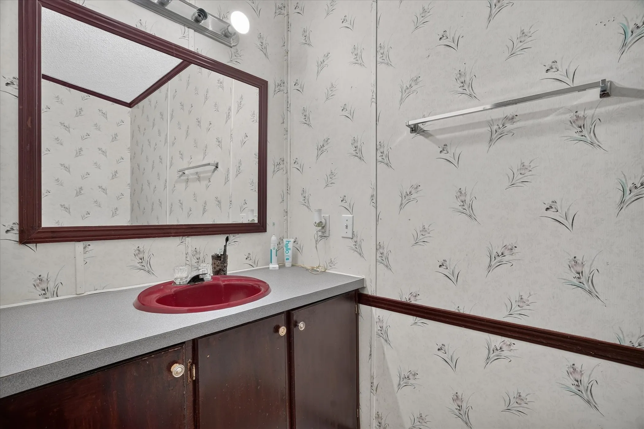 Vanity with a red basin, dark wood-finish cabinetry, and a light-colored countertop
