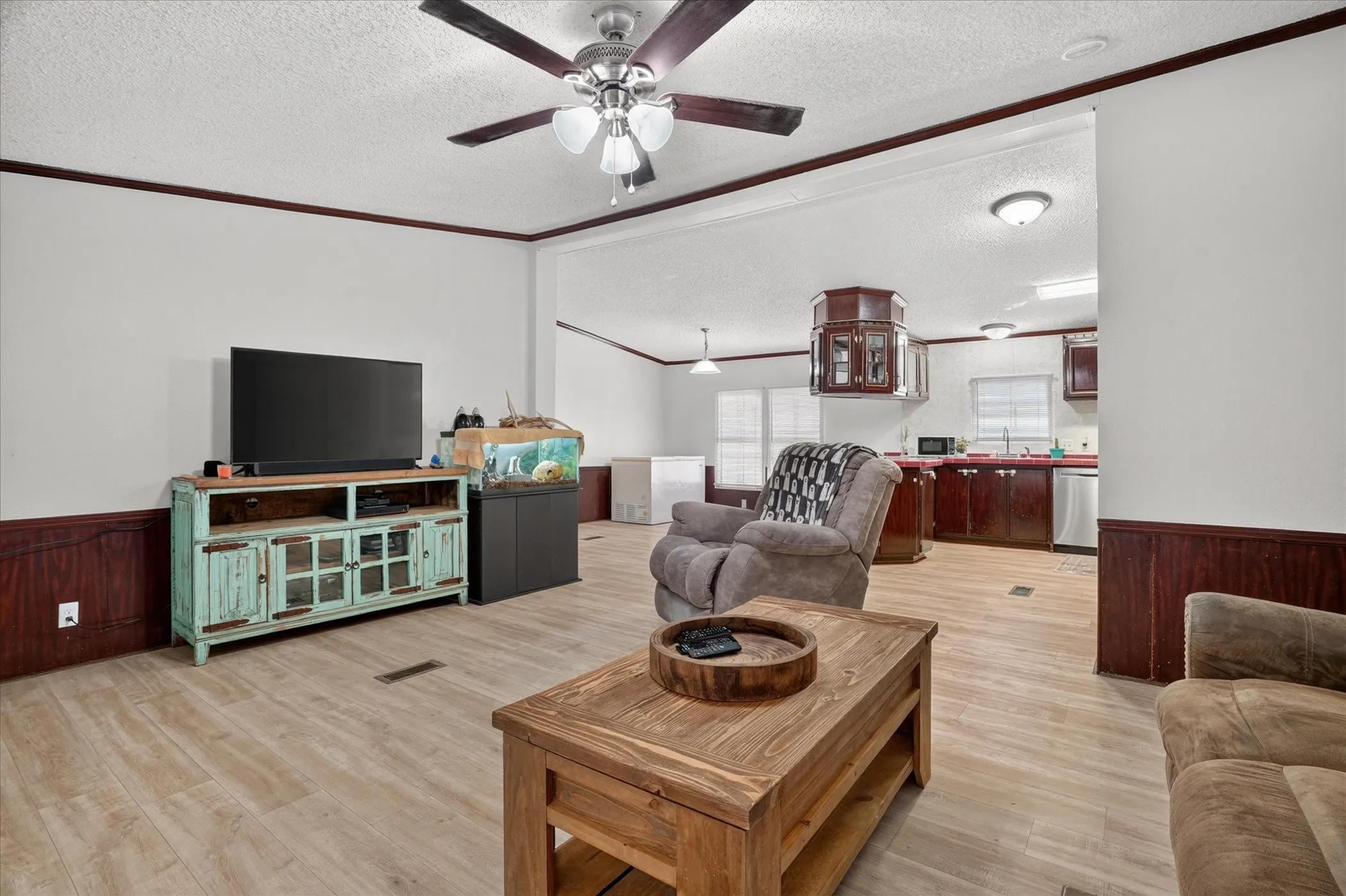 Open-concept living area with wood-finish flooring, dark wood wainscoting, and a ceiling fan with integrated lighting