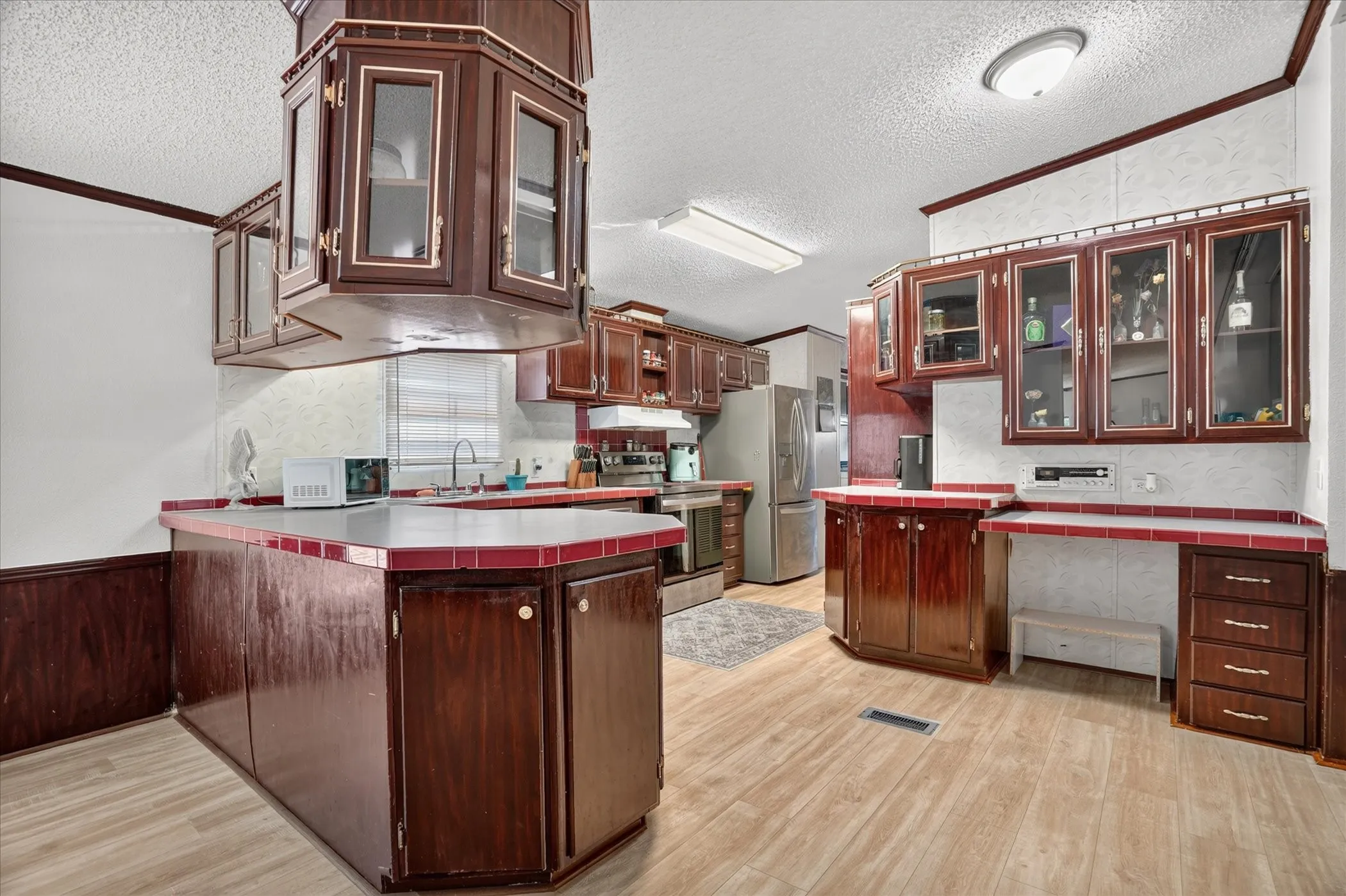Kitchen featuring wood-finish flooring, dark wood cabinetry, glass-front upper cabinets, and red tile countertops