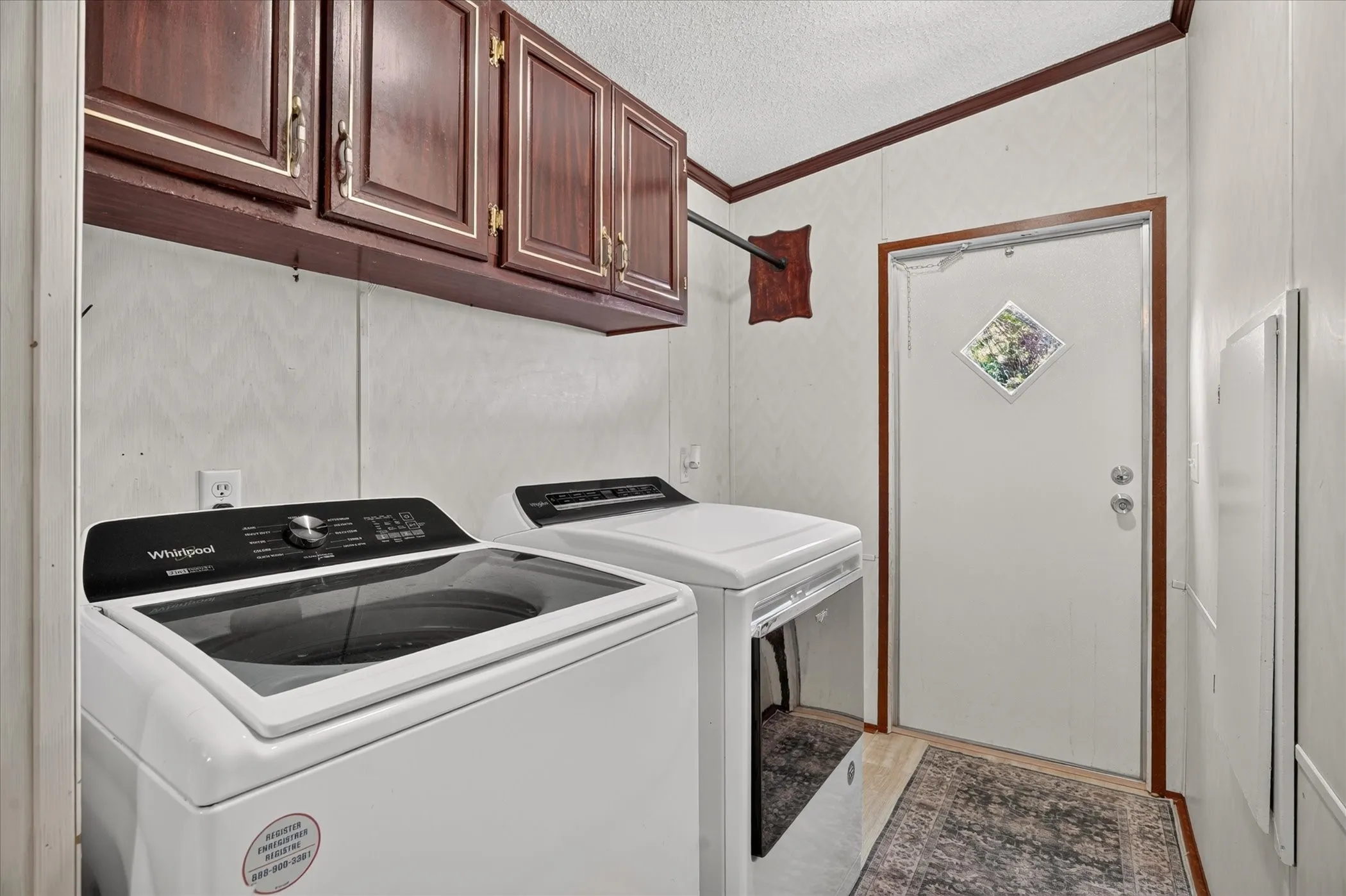 Laundry area featuring built-in wood-finish cabinetry and a white paneled door with decorative glass inlay