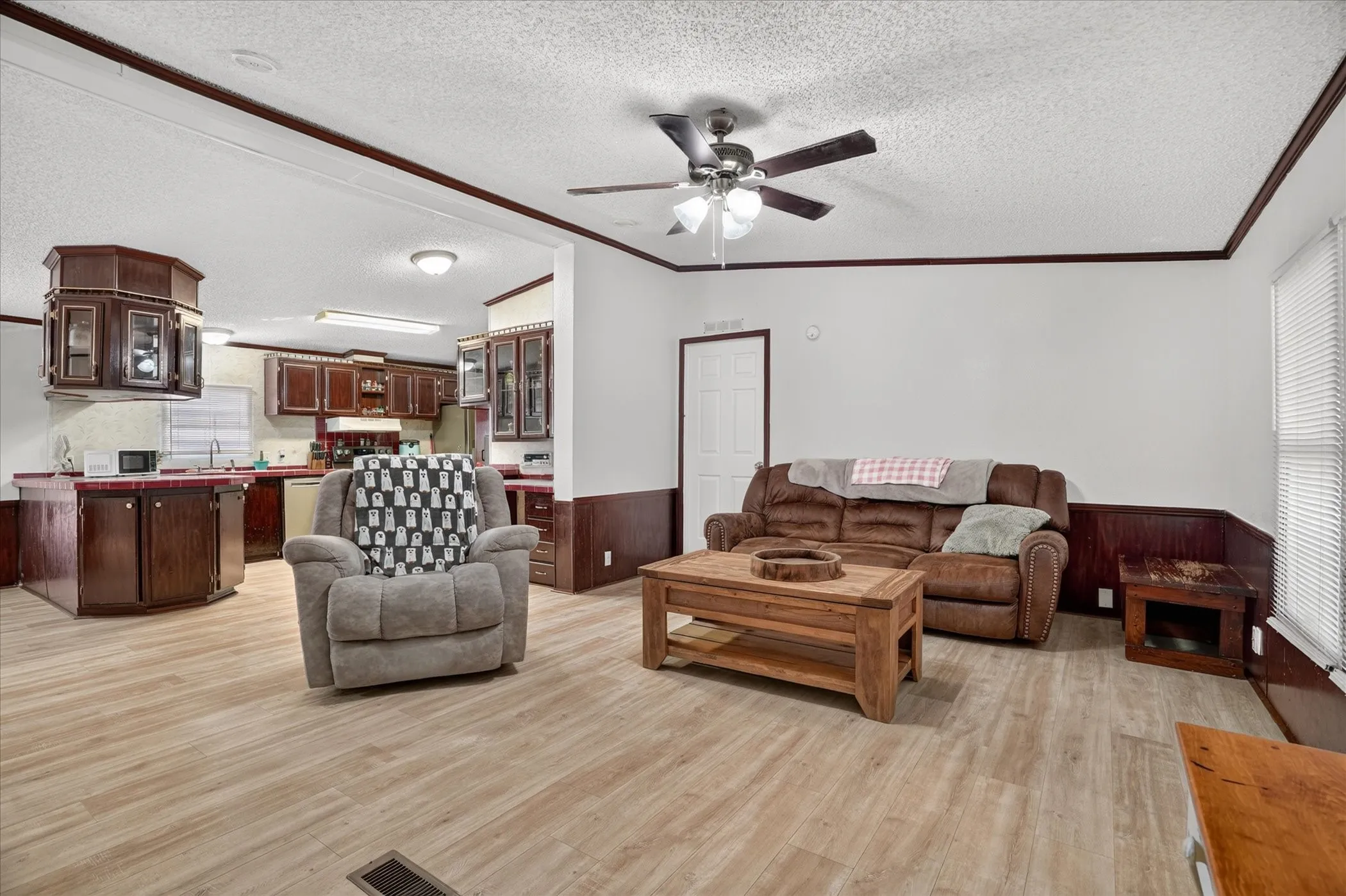 Open-concept living area with wood-finish flooring, a ceiling fan, and crown molding