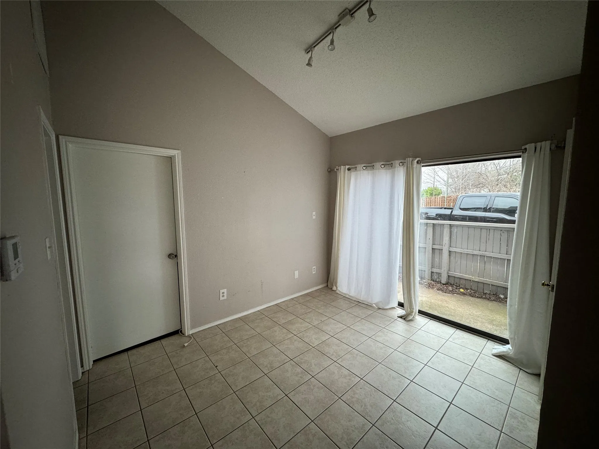Vaulted ceiling with track lighting, tile flooring, and sliding glass door access to a private outdoor space