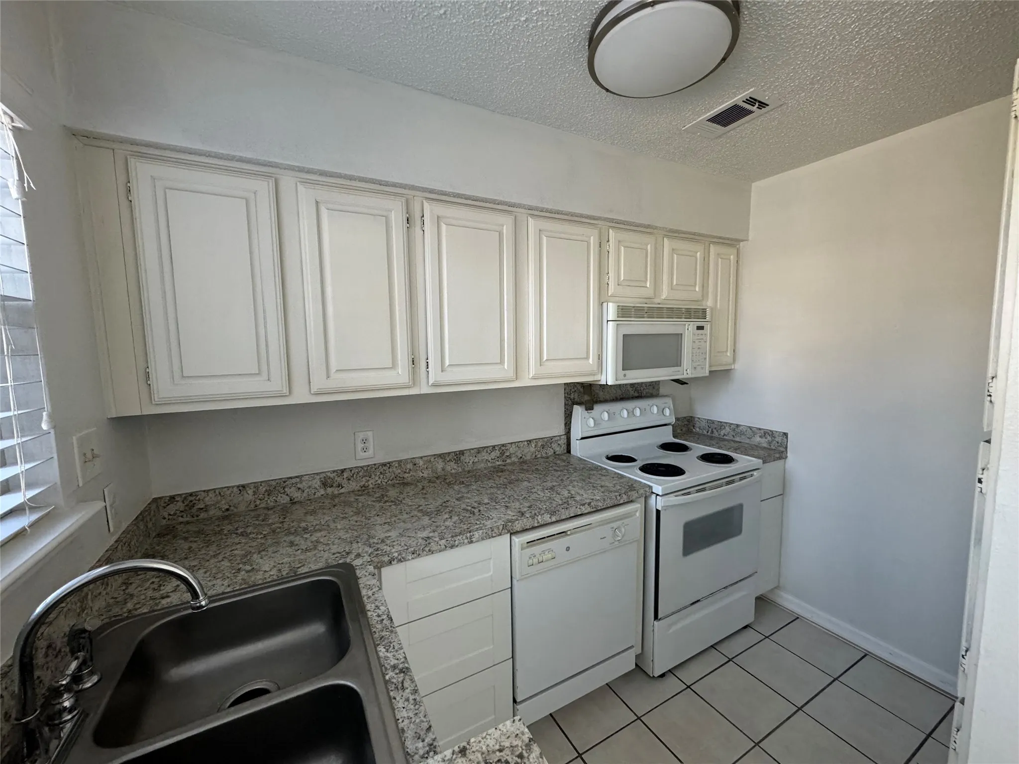 Kitchen with visible vents, light tile patterned floors, a sink, white appliances, and white cabinetry