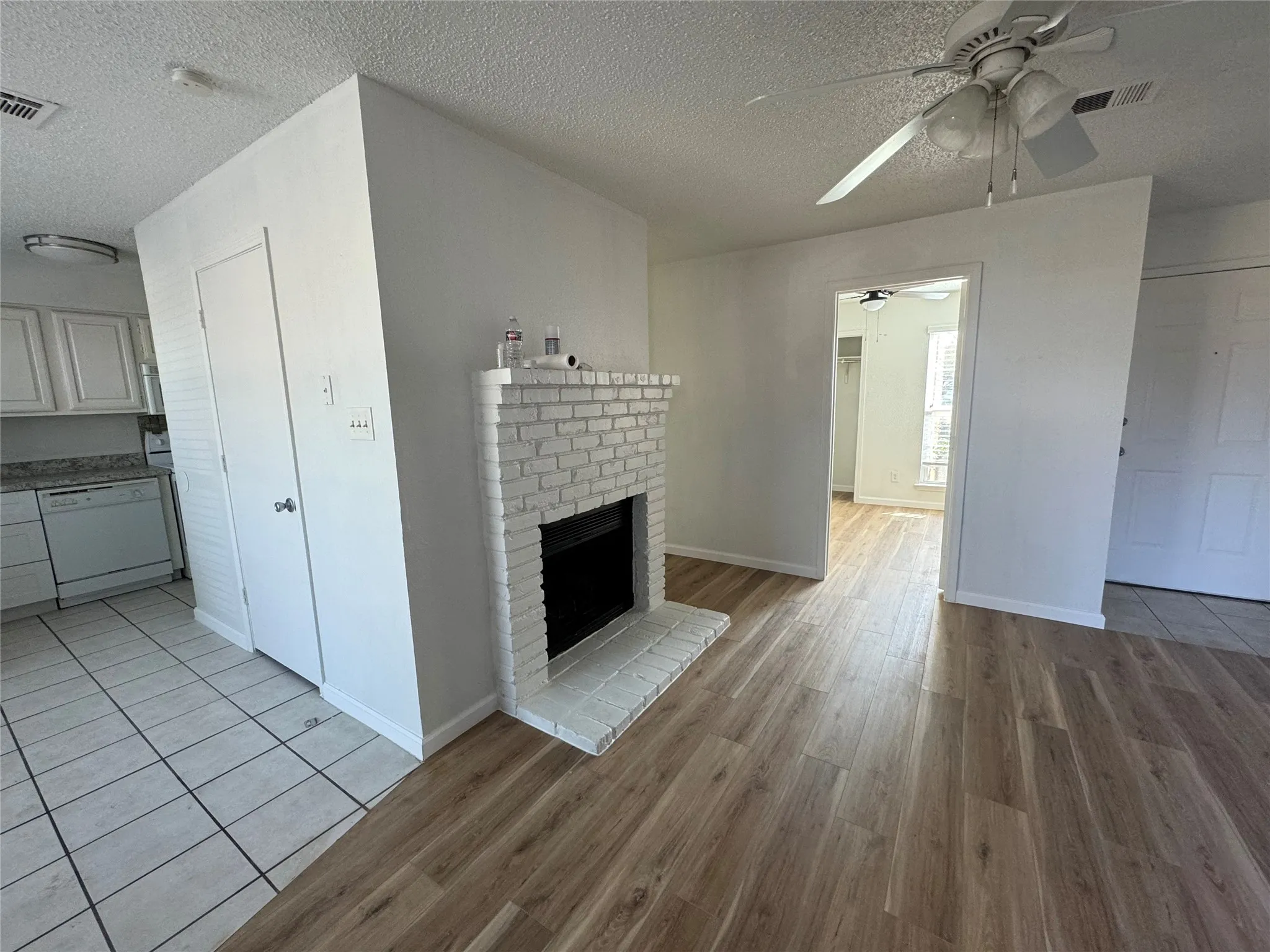 Unfurnished living room with visible vents, a ceiling fan, a textured ceiling, a fireplace, and light wood-style flooring