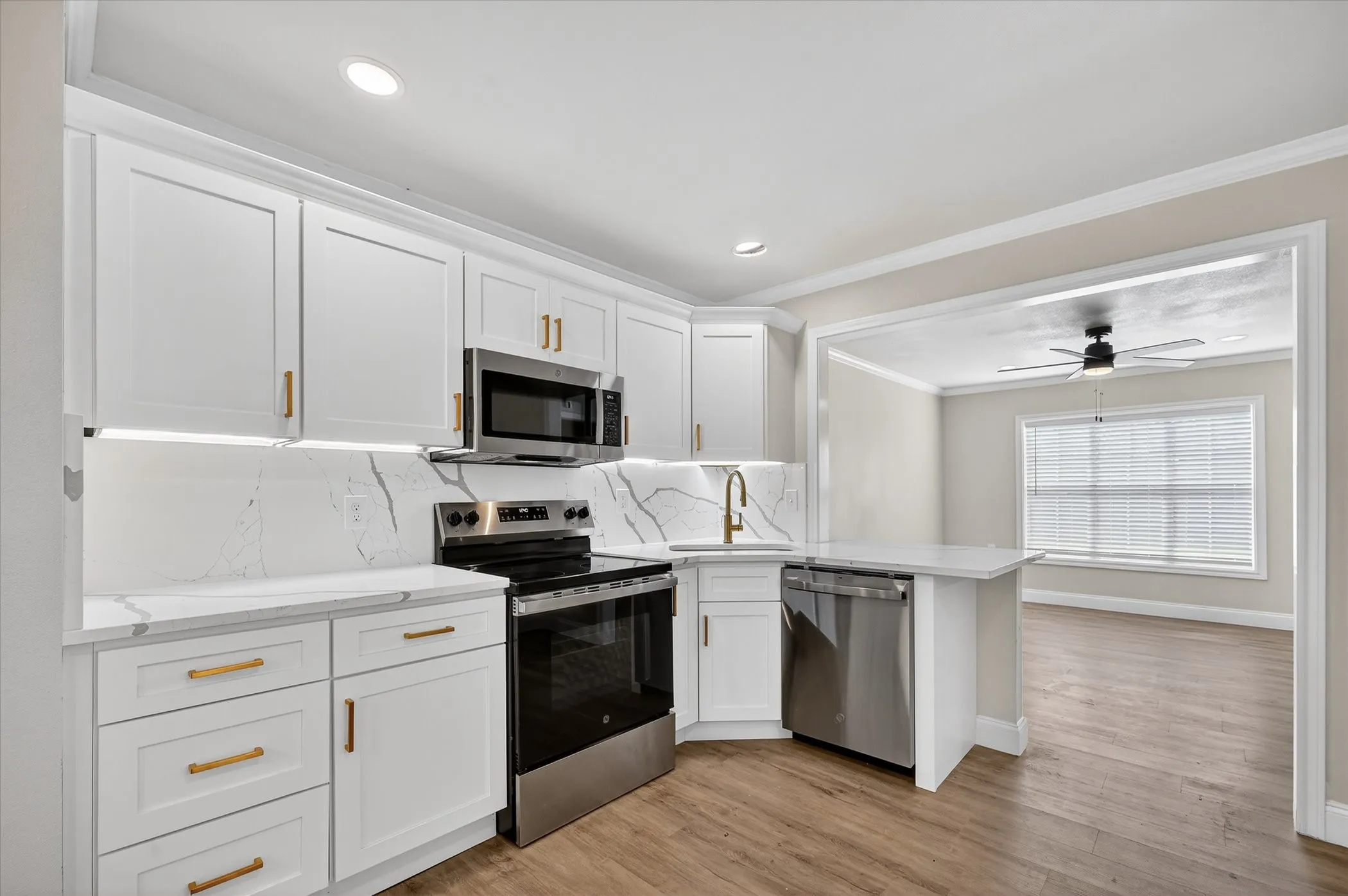 White shaker cabinetry, stainless steel appliances, white countertops with integrated backsplash, wood-finish flooring, and recessed lighting