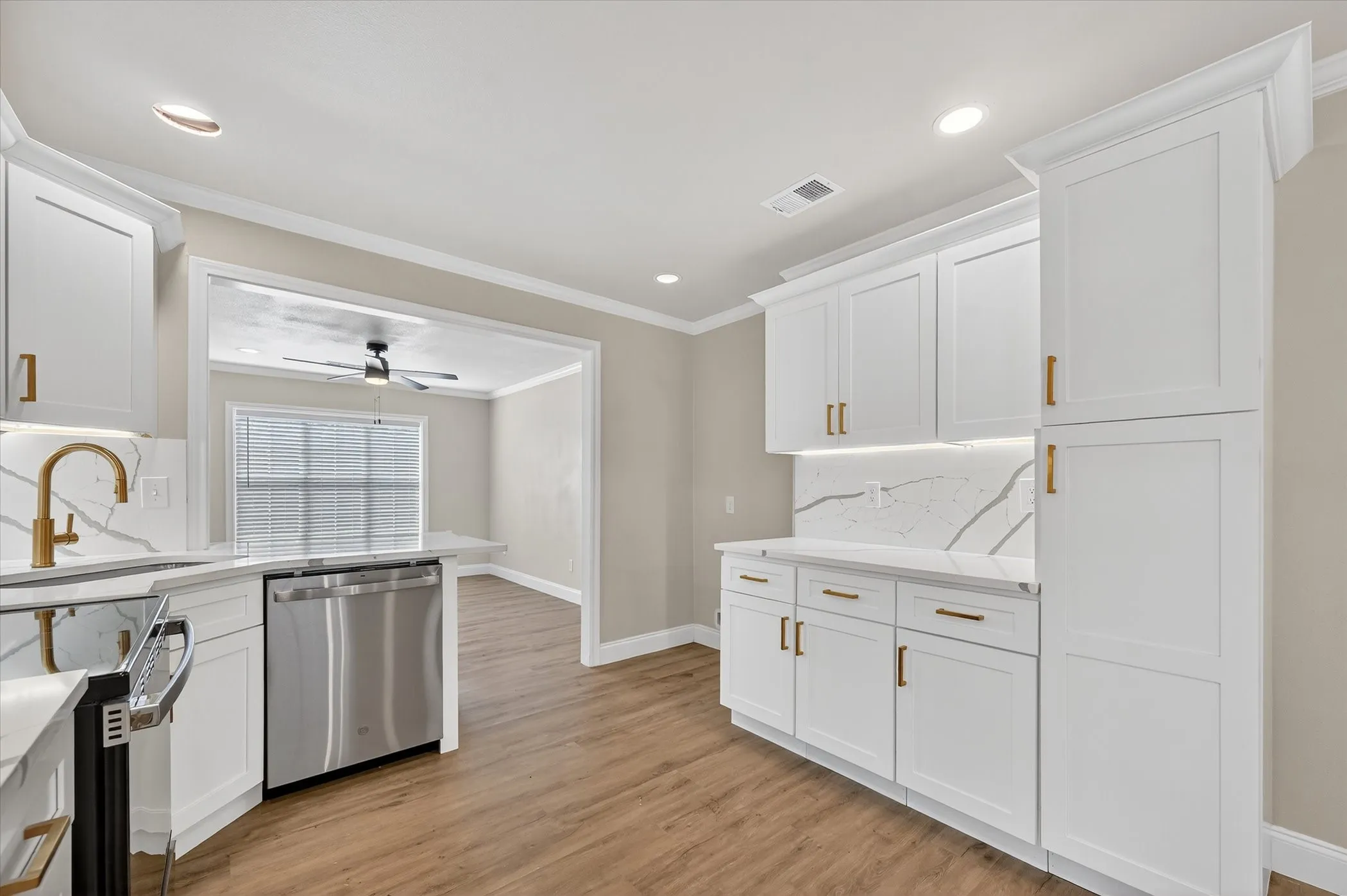 White shaker cabinetry with gold-tone hardware, full-height backsplash, undermount sink with gold-tone faucet, and wood-finish flooring