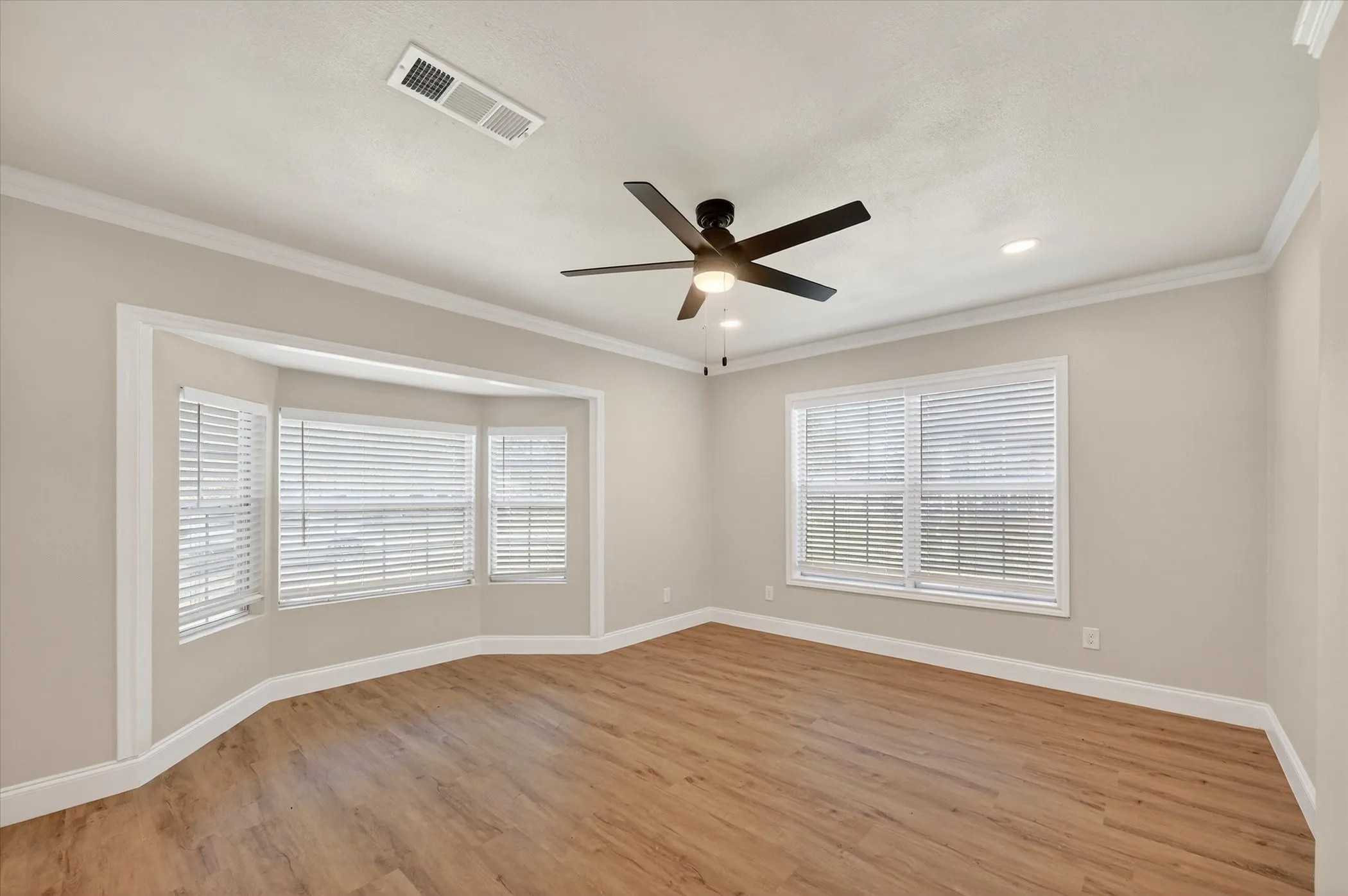 Wood-finish flooring, recessed lighting, ceiling fan, crown molding, and bay windows