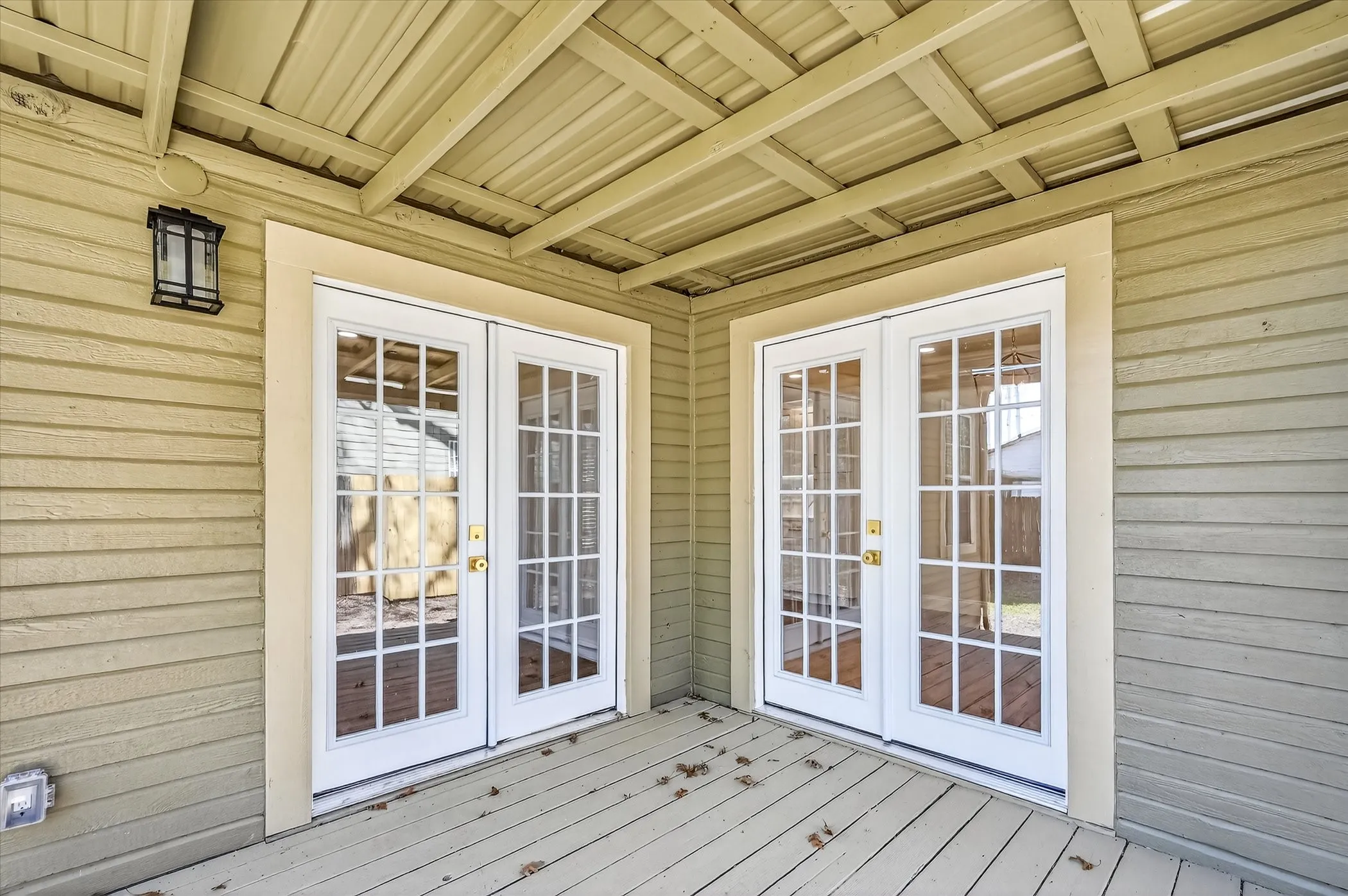 Covered outdoor deck with two sets of French doors, wood-finish flooring, and horizontal siding
