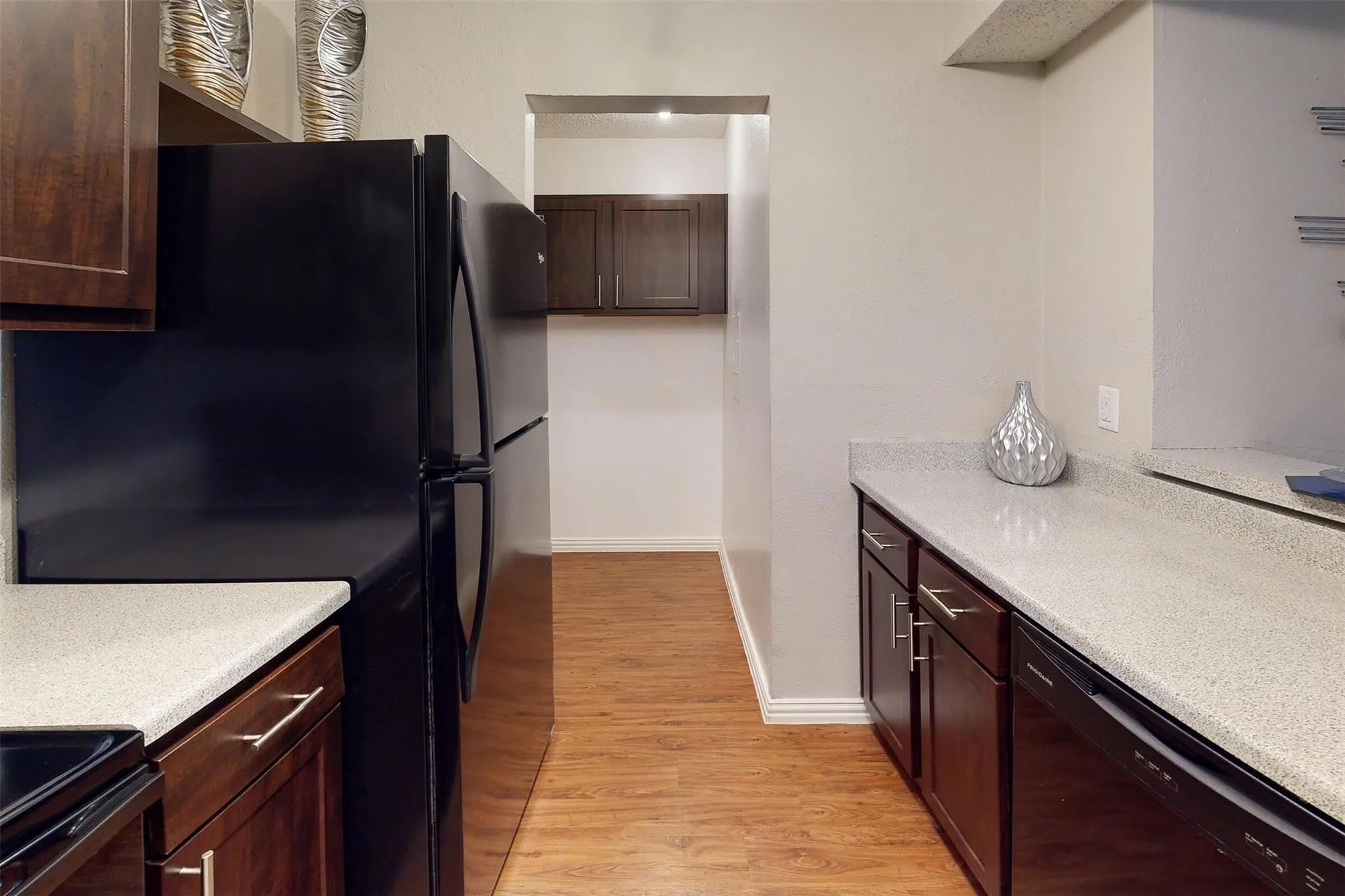Kitchen featuring wood-finish flooring, dark wood-finish cabinetry, light speckled countertops, and black appliances