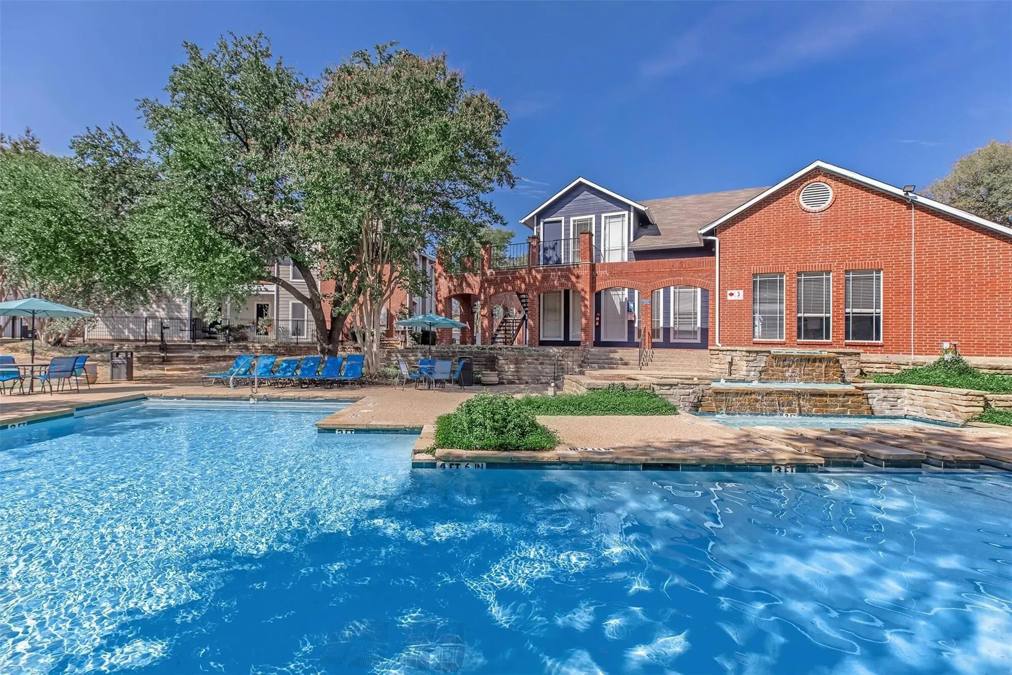 Swimming pool with concrete decking, a multi-tiered water feature, and brick building exterior