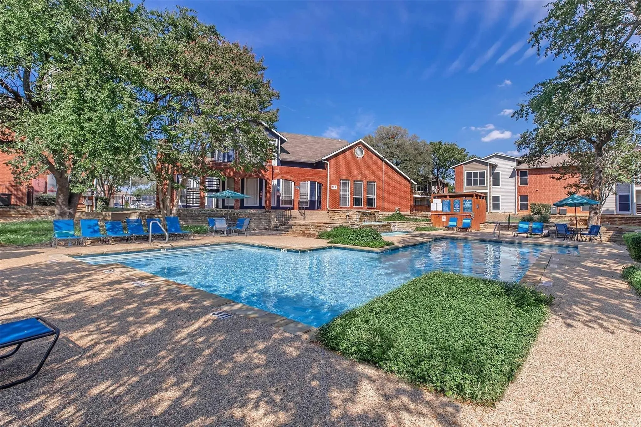 Two-tiered outdoor swimming pool with surrounding aggregate concrete decking and integrated landscaping