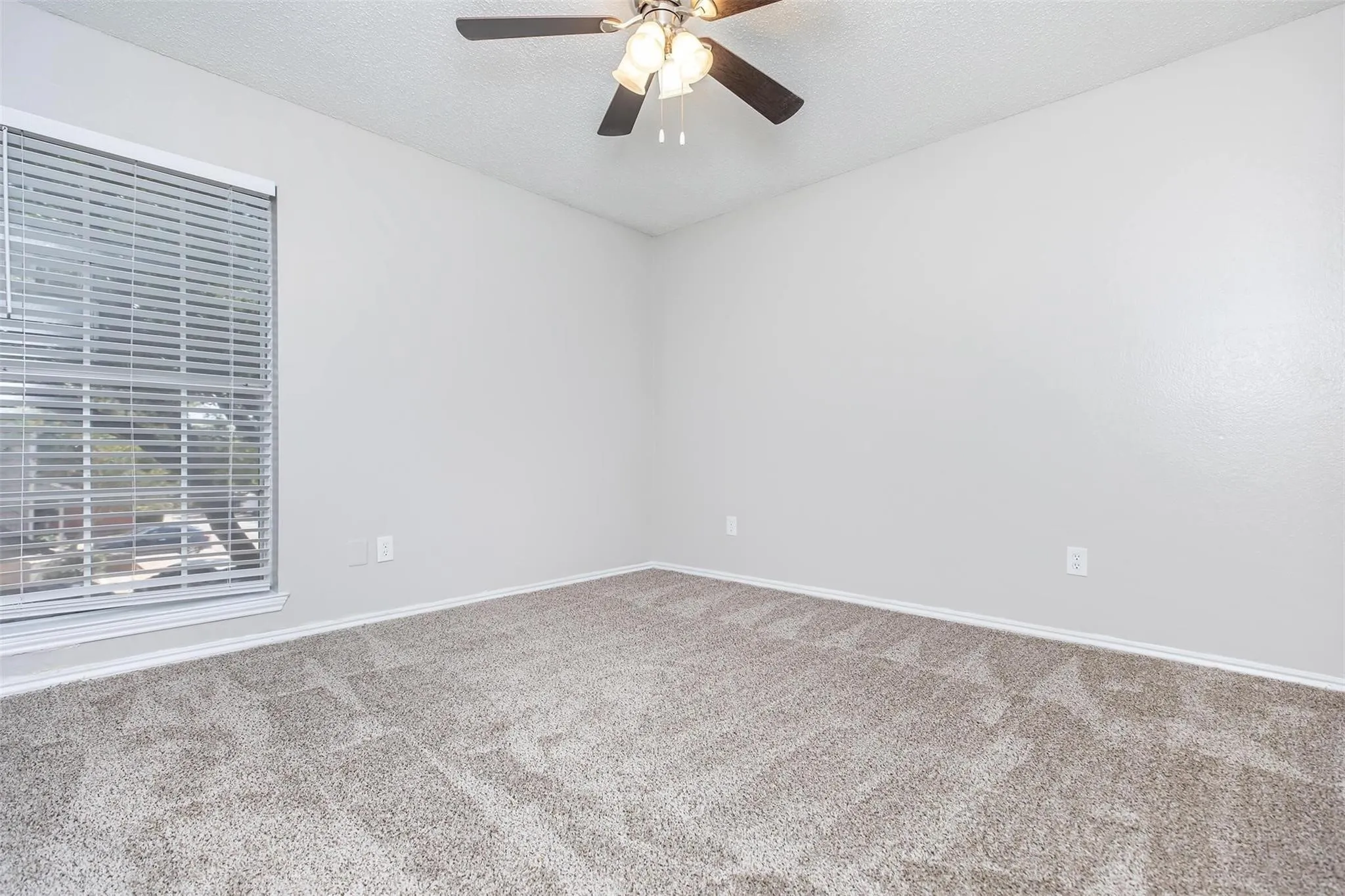 Plush carpet flooring, neutral wall tones, ceiling fan with integrated lighting, and window with horizontal blinds